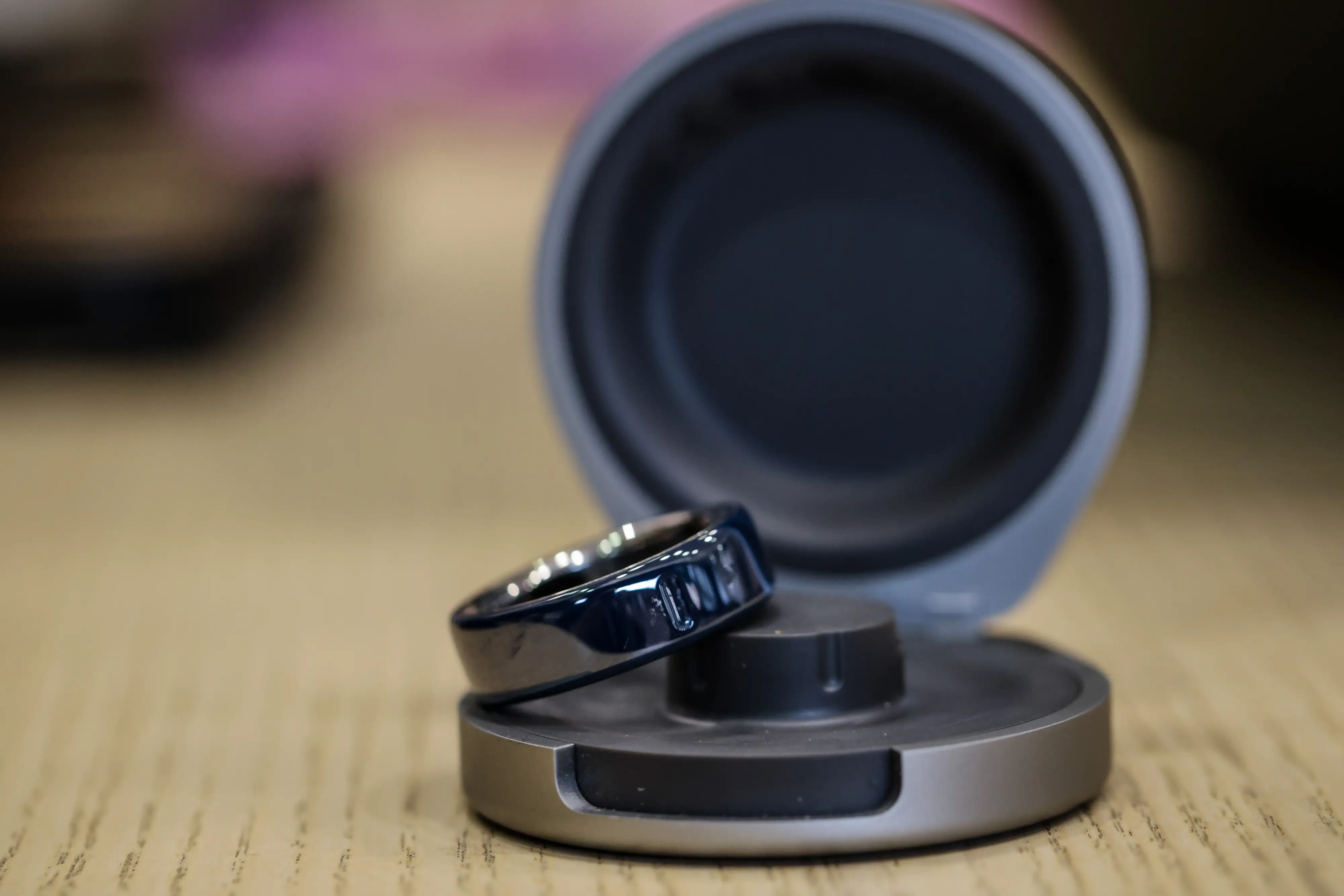 Glossy black smart ring rests on an open charging case on a wooden surface.