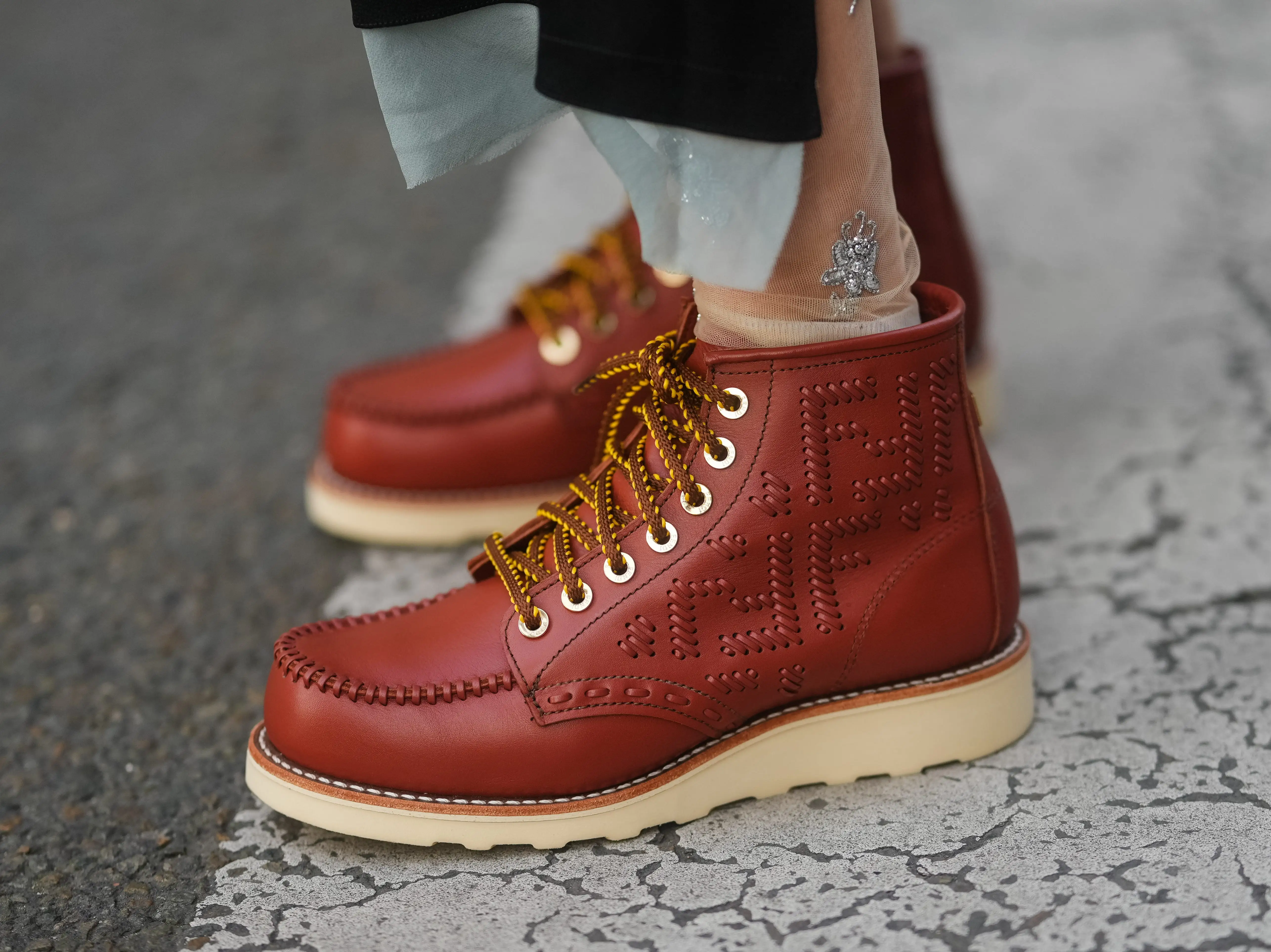 A pair of rust-colored leather boots with hiking-style laces and white rubber soles.