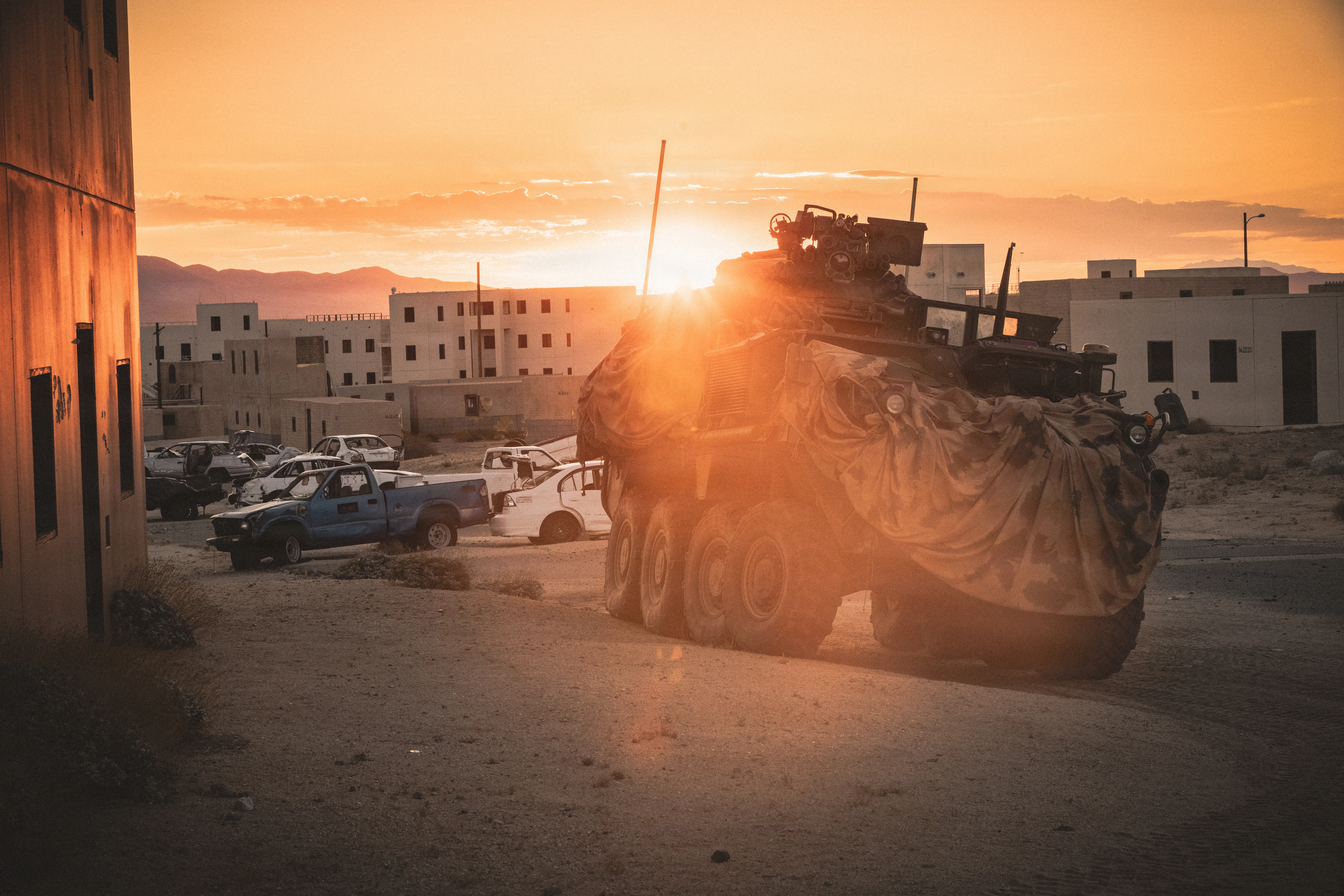A US Army Bradley Fighting Vehicle is parked near a fake urban city and totaled cars.