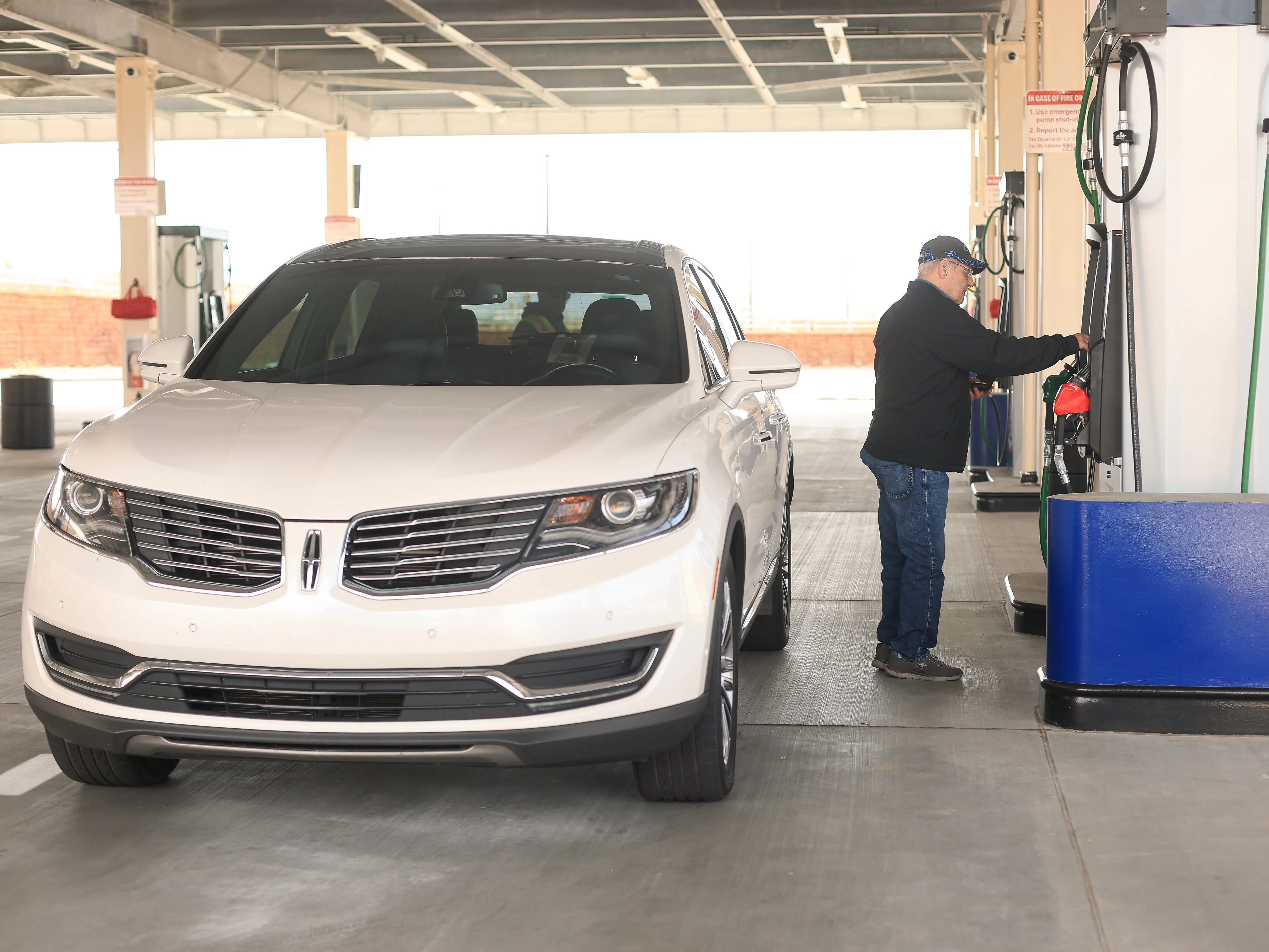 A man pays at a gas station, next to a white SUV.