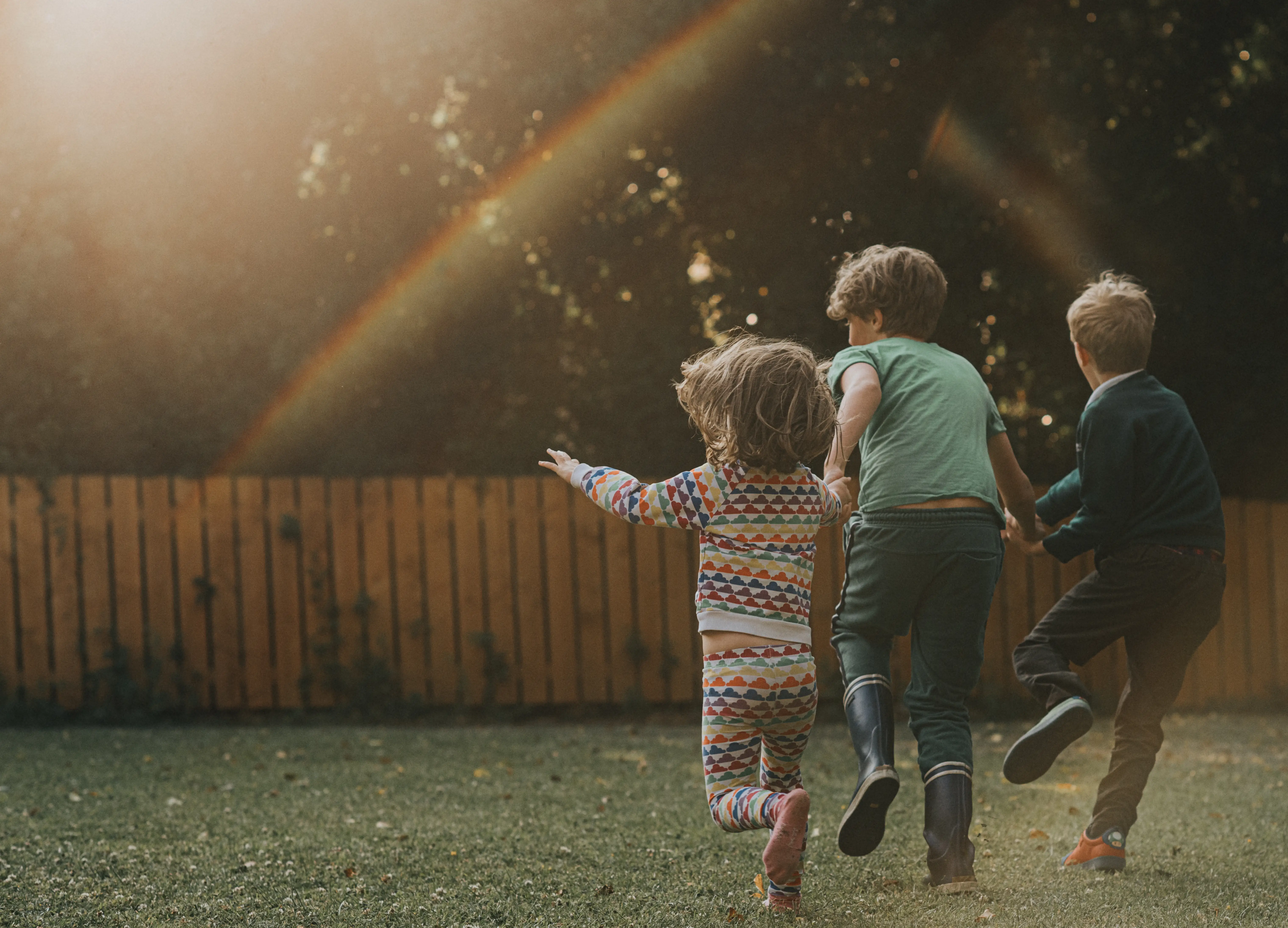 three kids playing in a backyard, there's a rainbow from the light on the lens