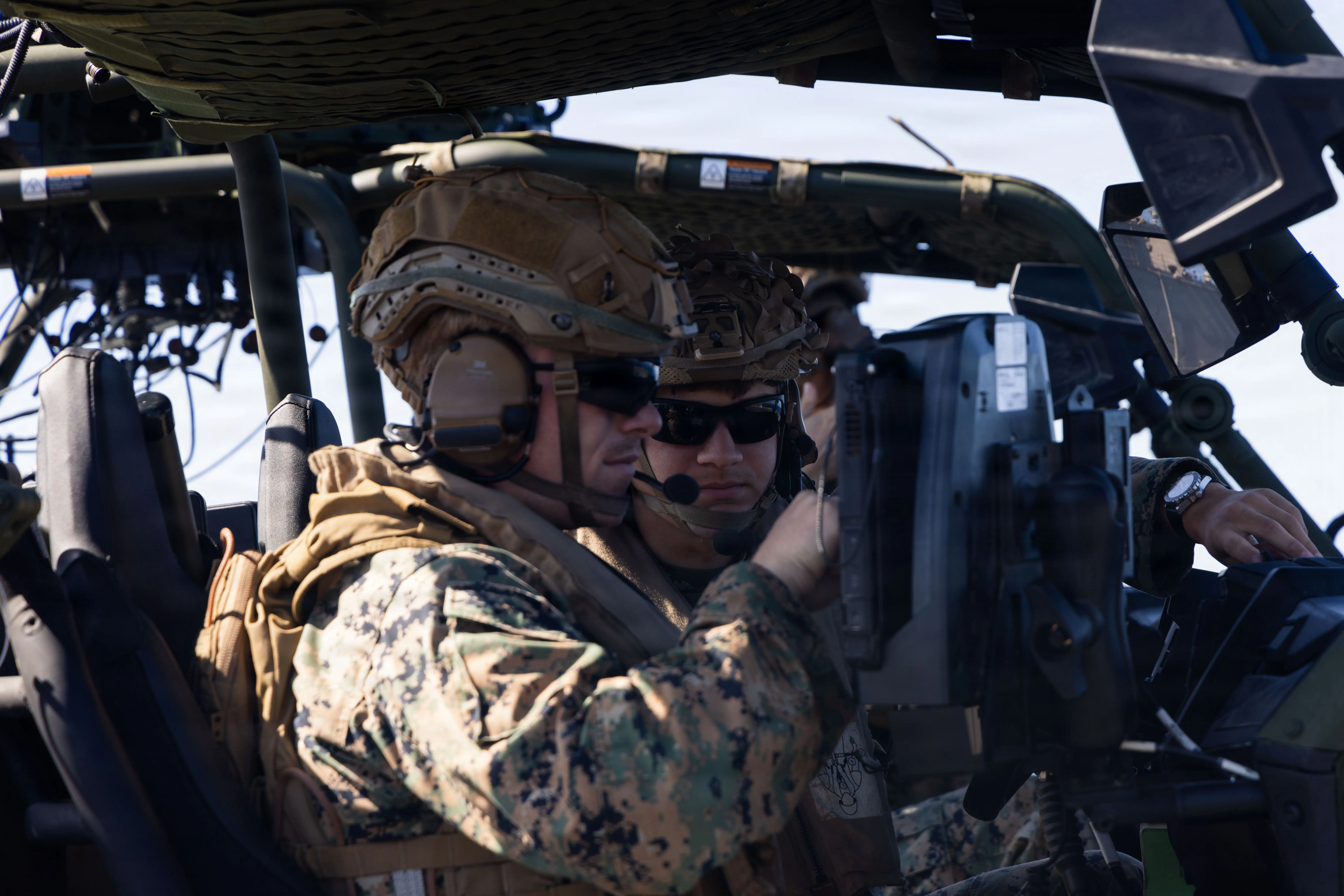 Two helmeted service members in camouflage operate equipment inside a vehicle.