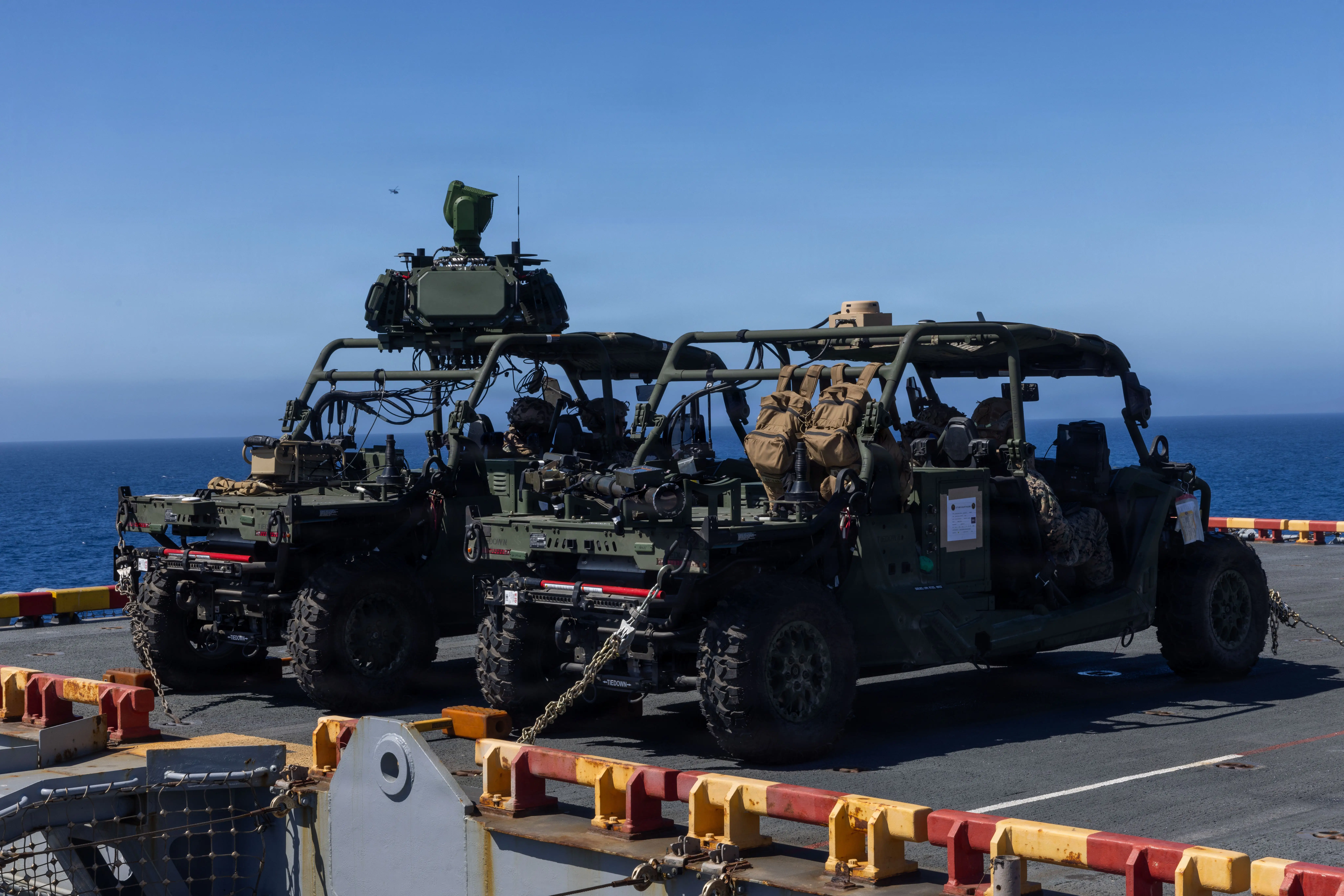 Two military utility vehicles are parked on a ship deck with the ocean visible in the background.
