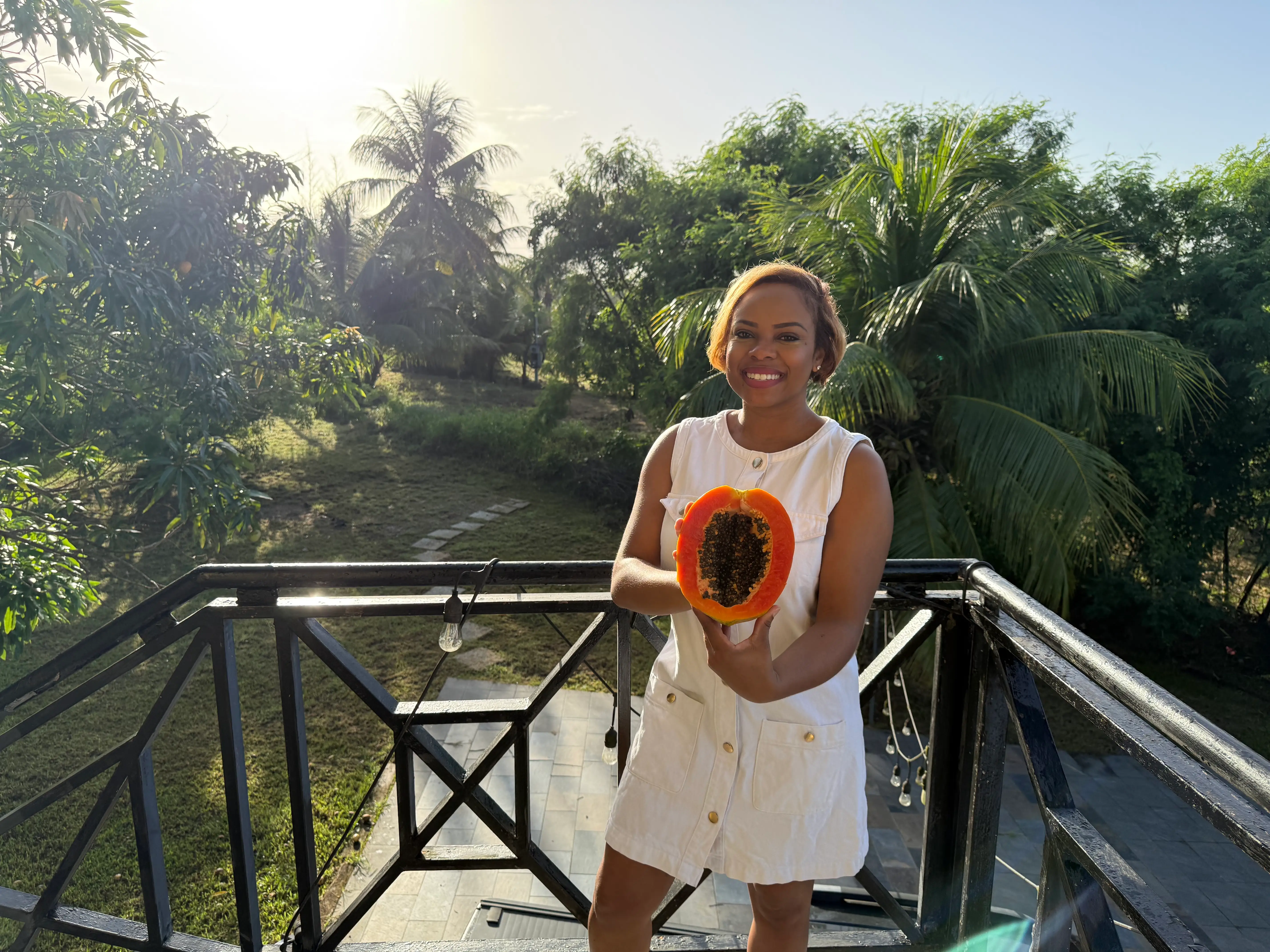 Woman smiling holding fruit with trees behind her