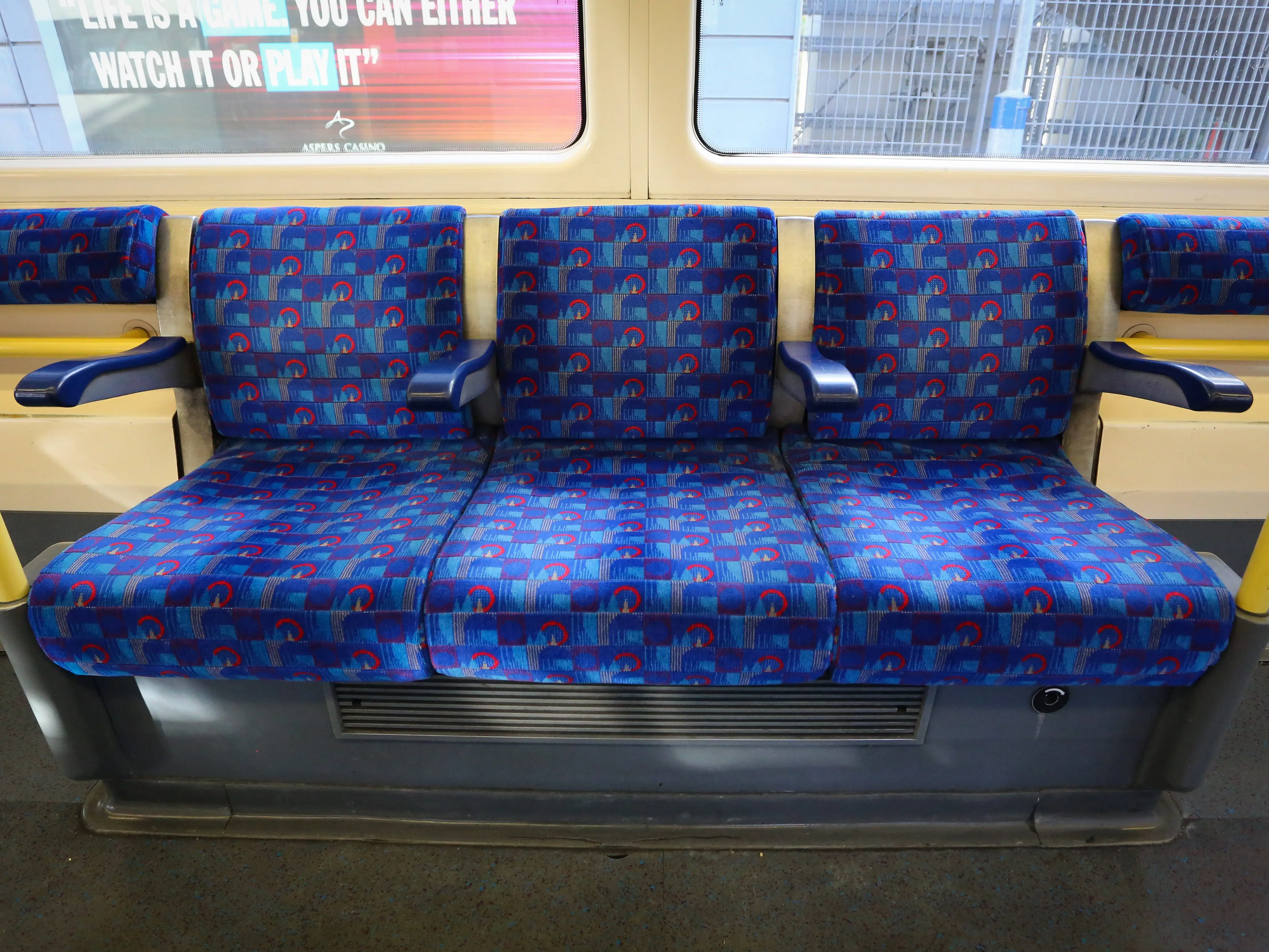 Empty blue patterned bench seats line the interior of a public transit train carriage.