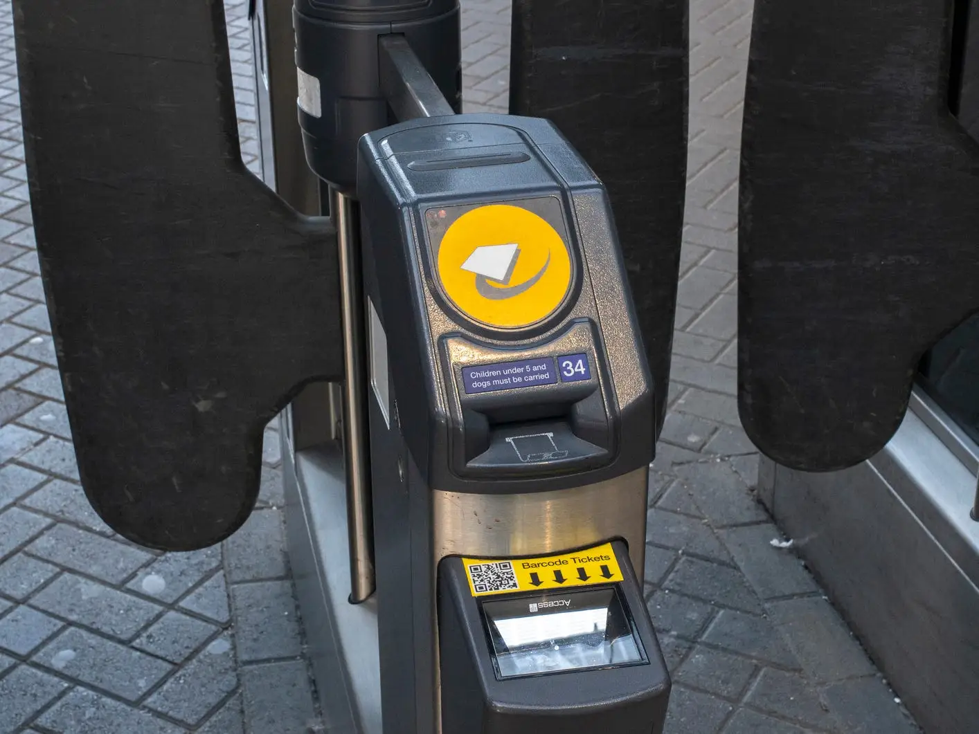 Contactless transit card reader and black ticket barriers stand at a rail station entrance.