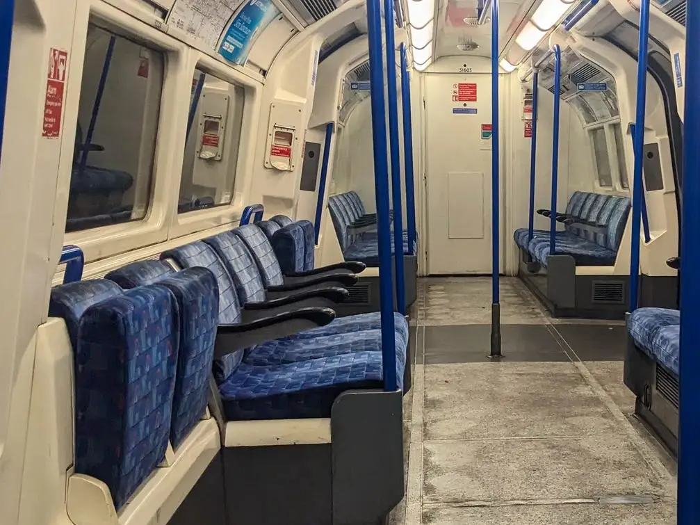 Empty underground train carriage with blue seats, blue poles, route maps, and advertising panels inside.