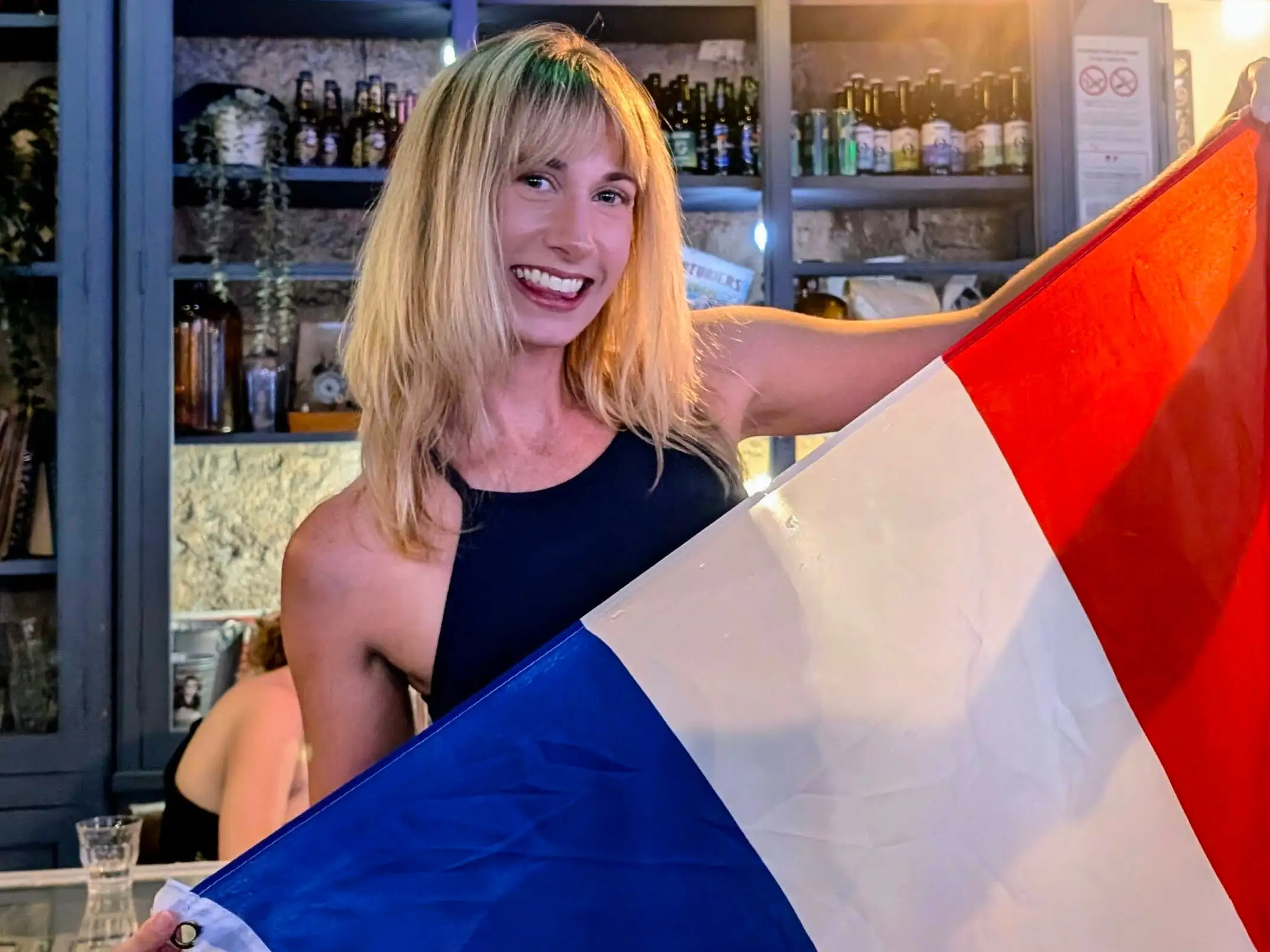 Leah Young smiles while holding a French flag inside a bar.