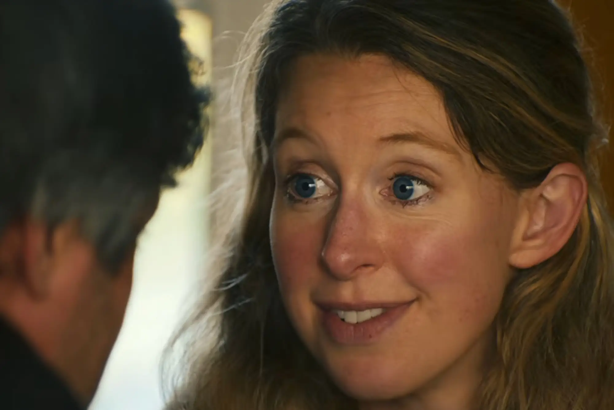 Elizabeth Holmes grins with her blue eyes wide open.
