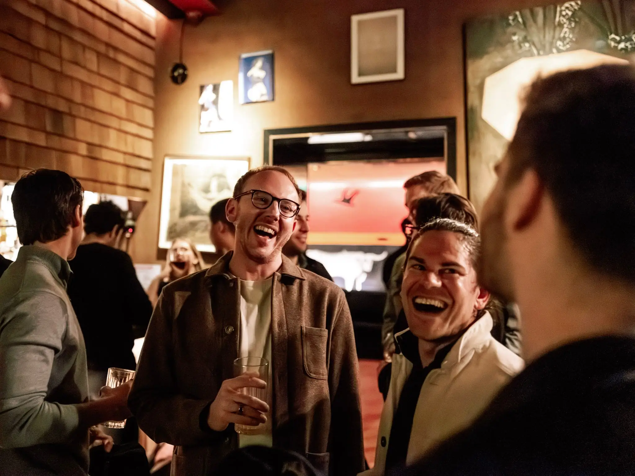 Erick Rabin and Matt Holbreich laugh and socialize with drinks in a warmly lit crowded bar or lounge.