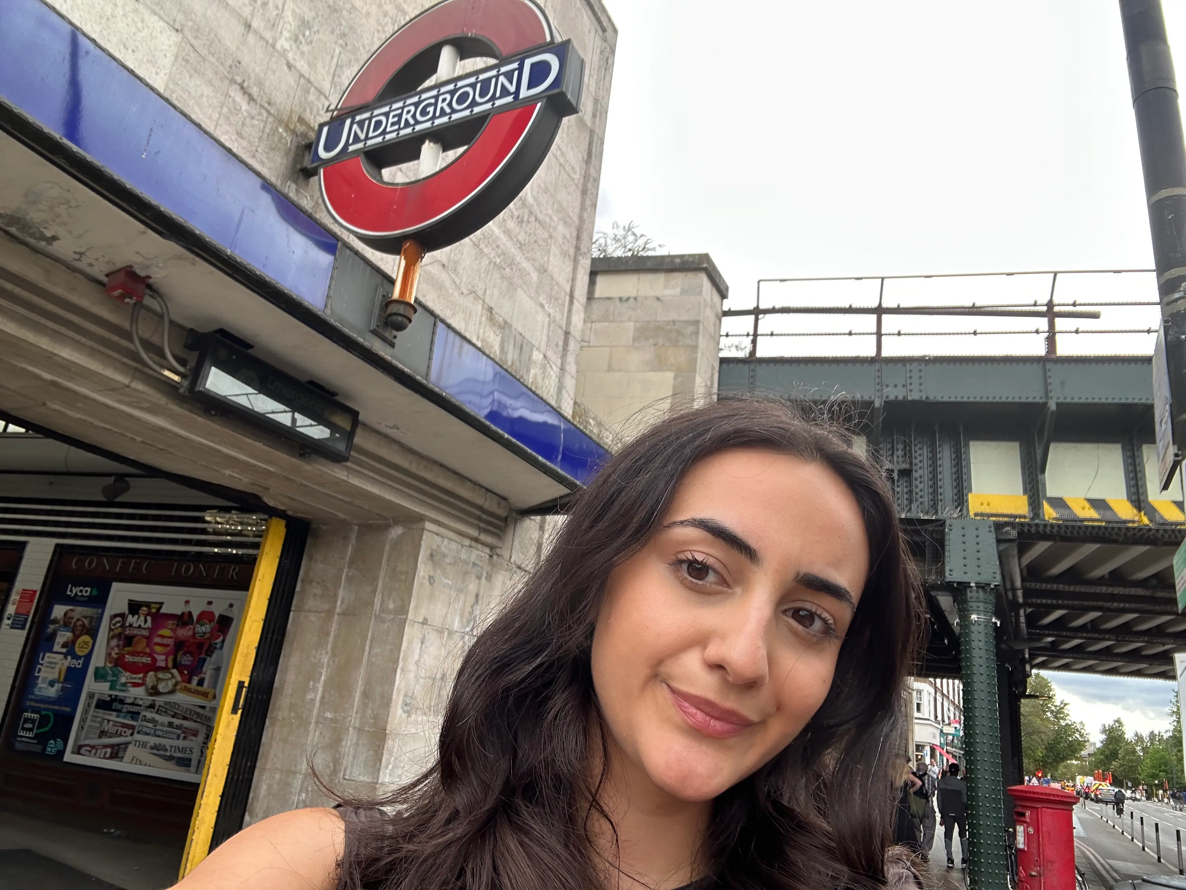 A person takes a selfie outside a London Underground entrance beside an elevated railway bridge.