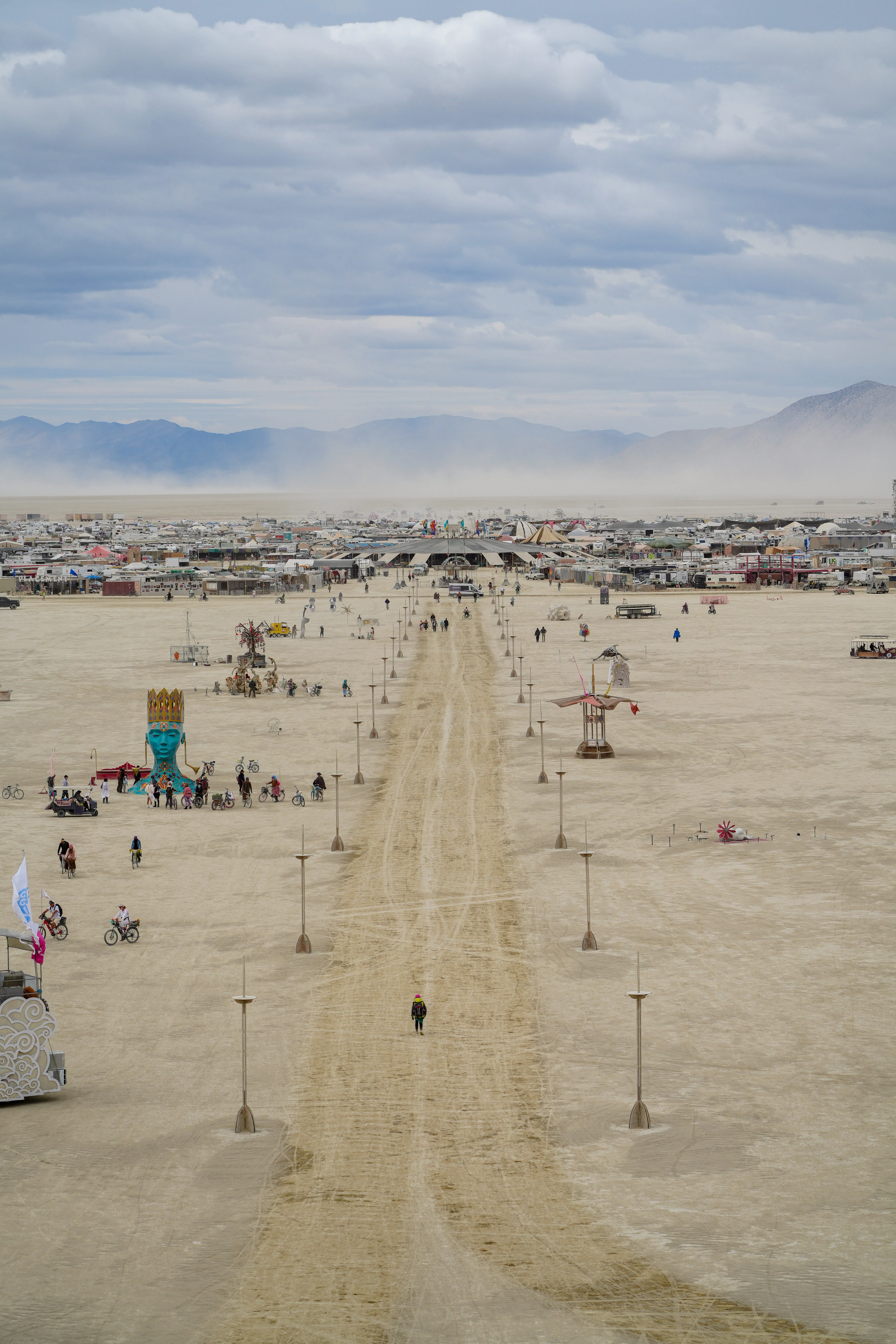 A broad desert festival site with art installations, vehicles, camps, and dusty mountains.