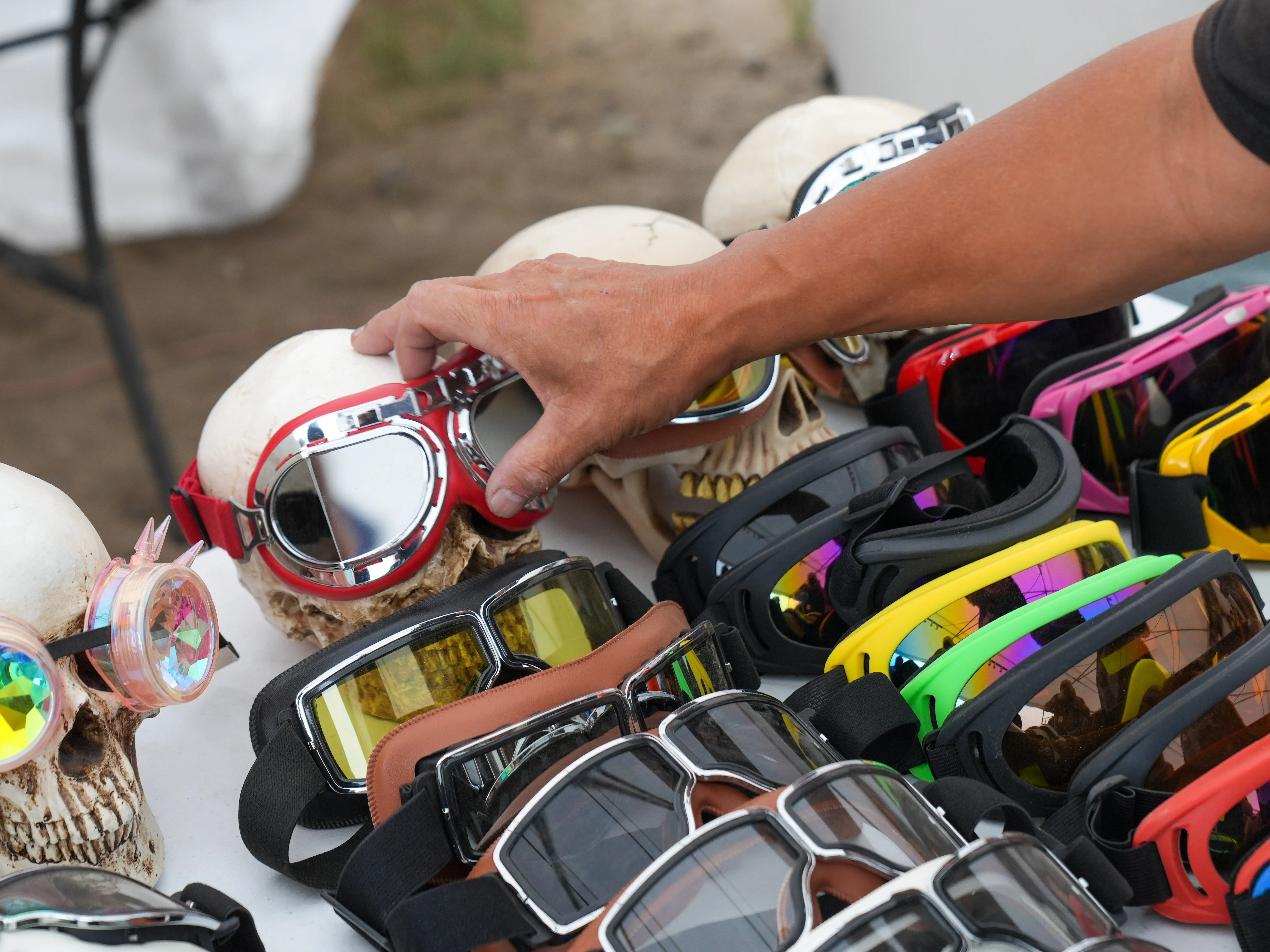 A hand reaches toward skull-shaped displays wearing goggles among rows of colorful eyewear.