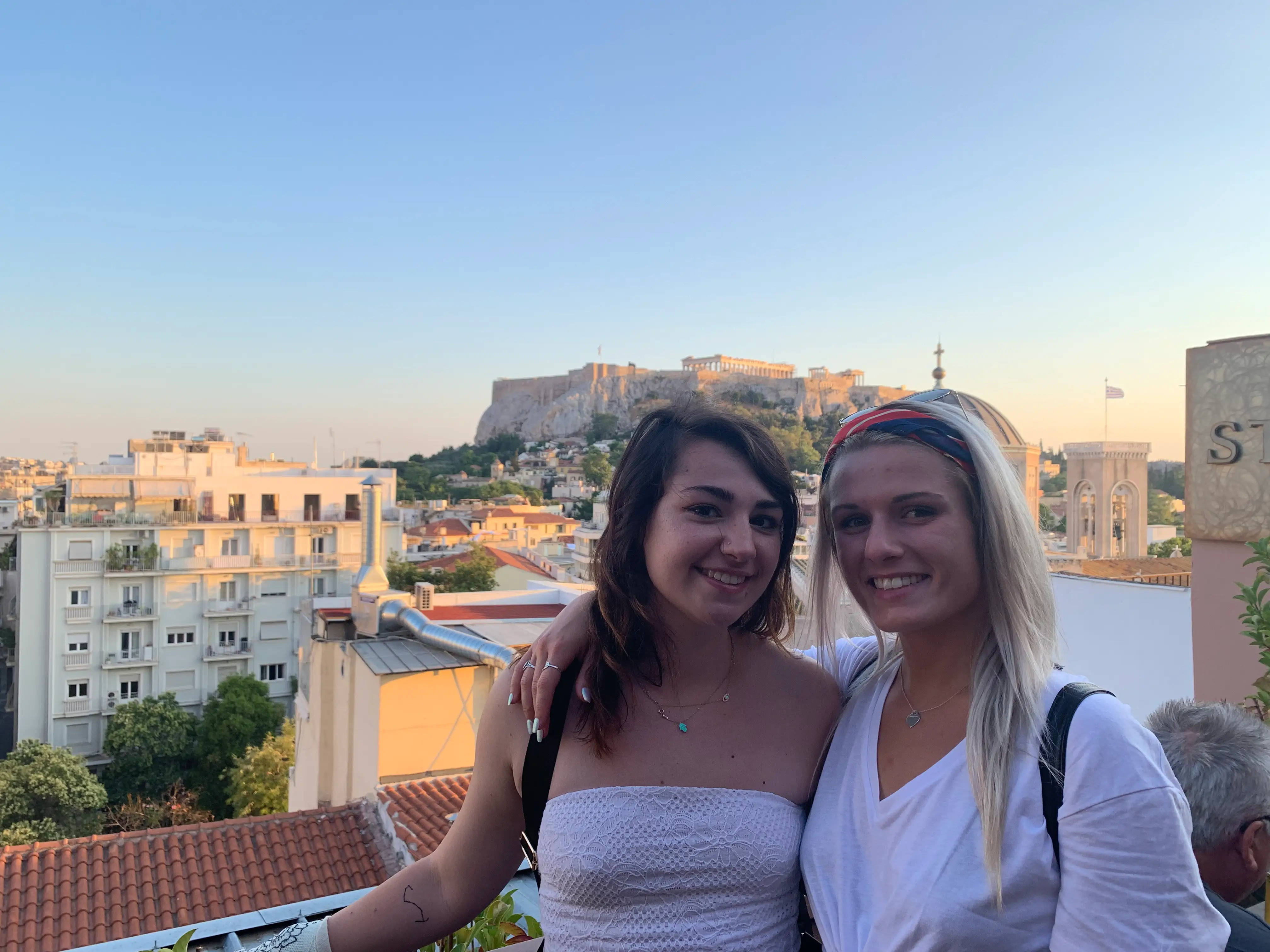 Two friends admire the Acropolis in Greece from a Plaka rooftop.