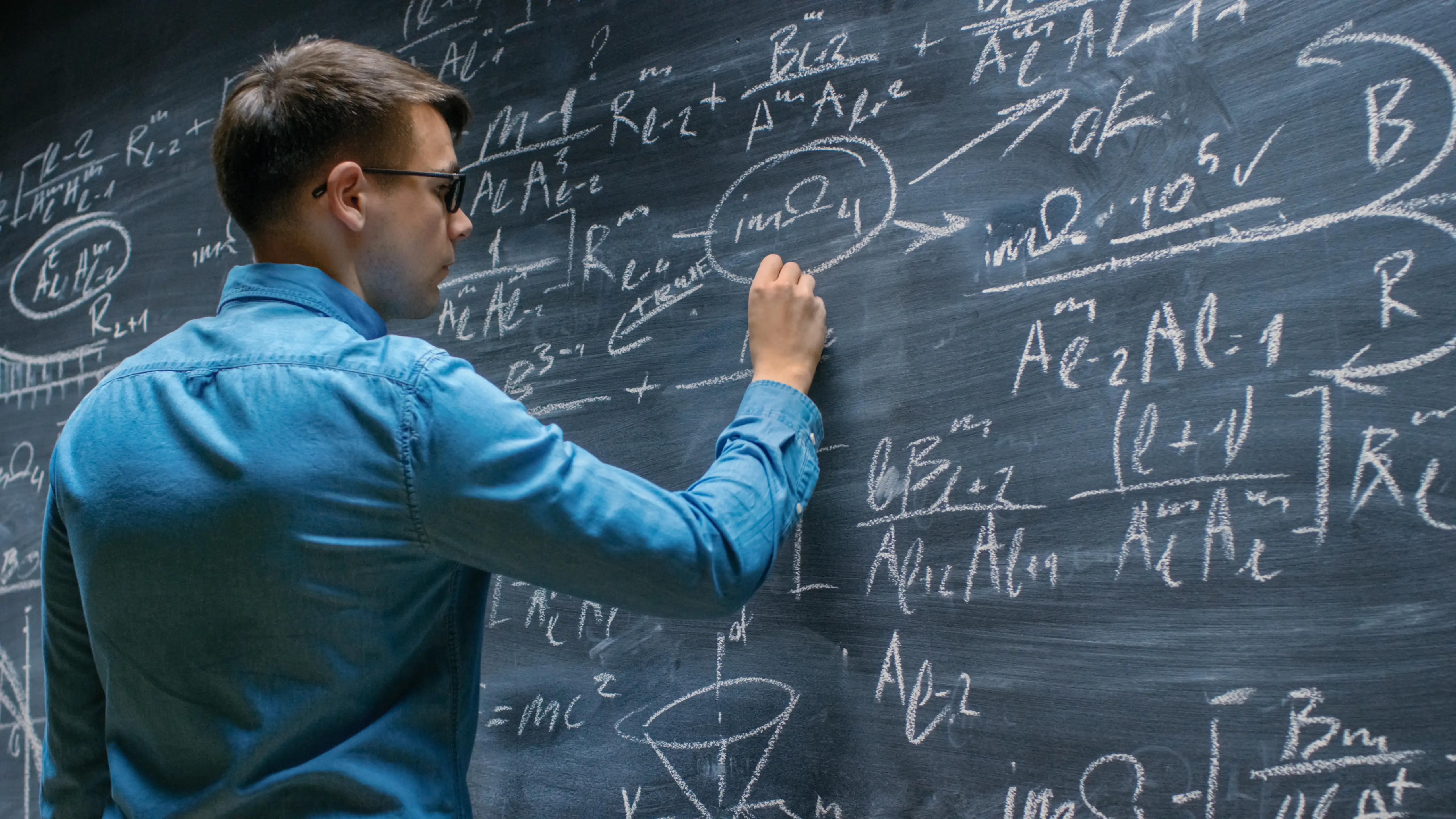 A mathematician writes equations on a chalkboard.