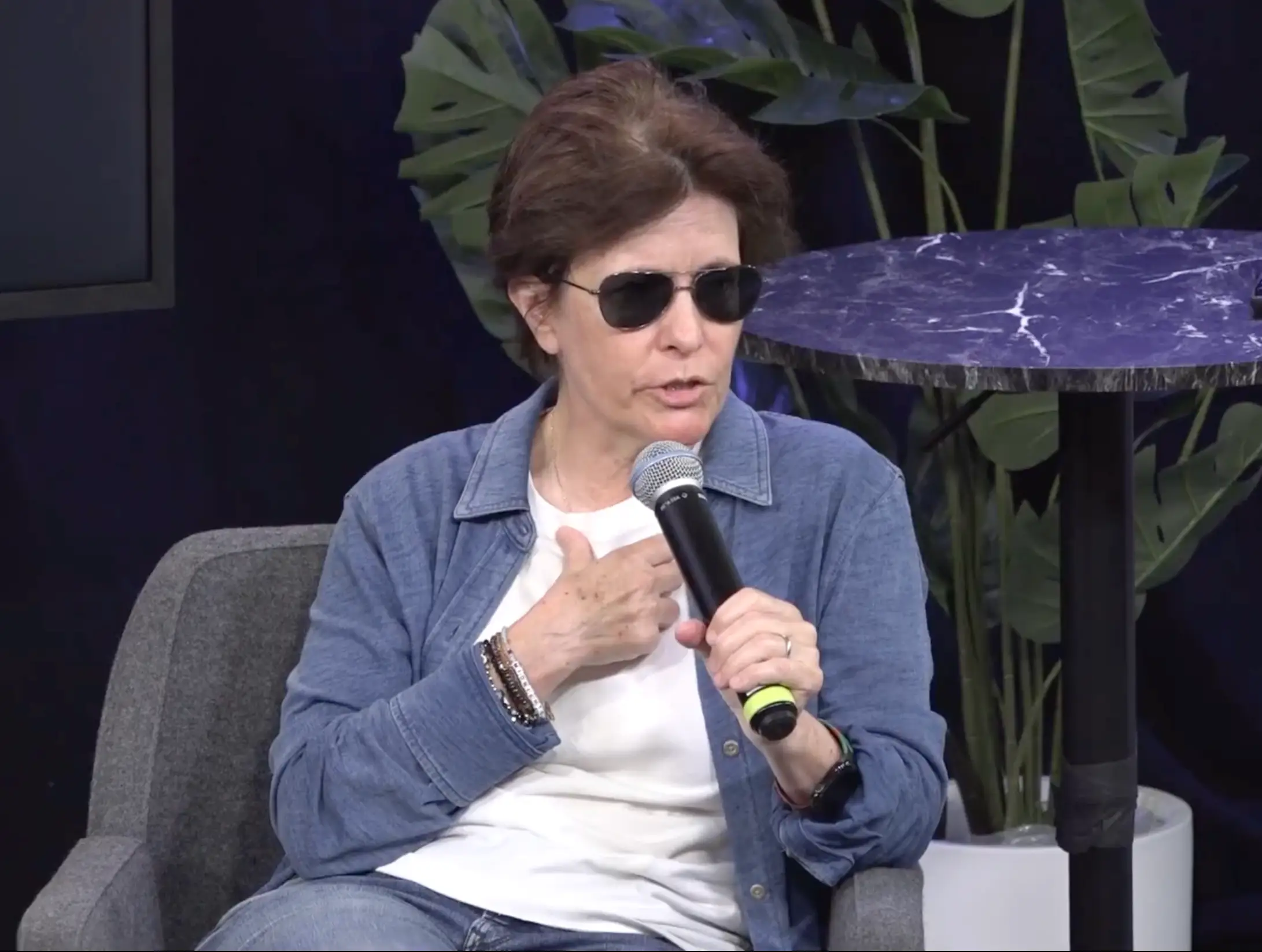 Kara Swisher speaking into a mic sitting on grey chair