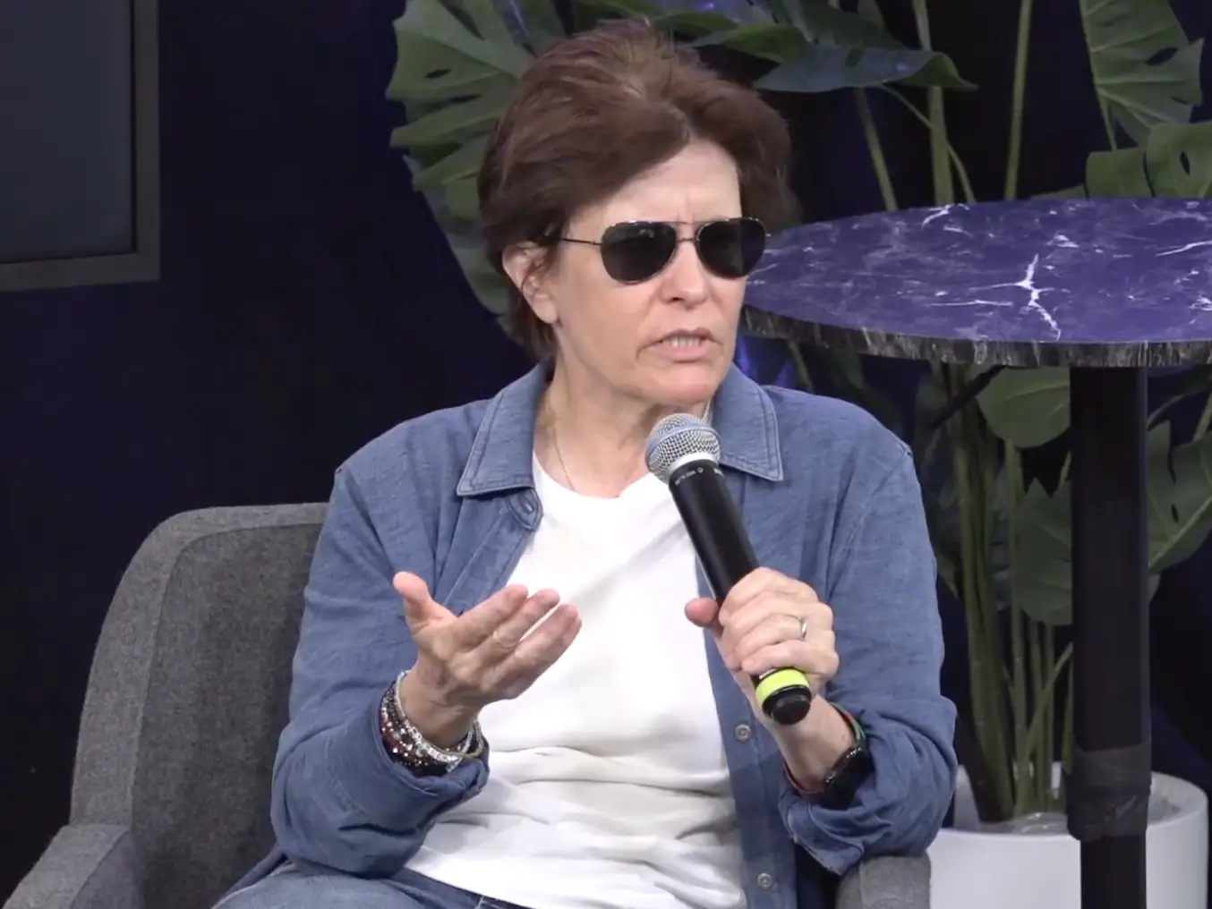 Kara Swisher speaking with a microphone, seated on grey chair