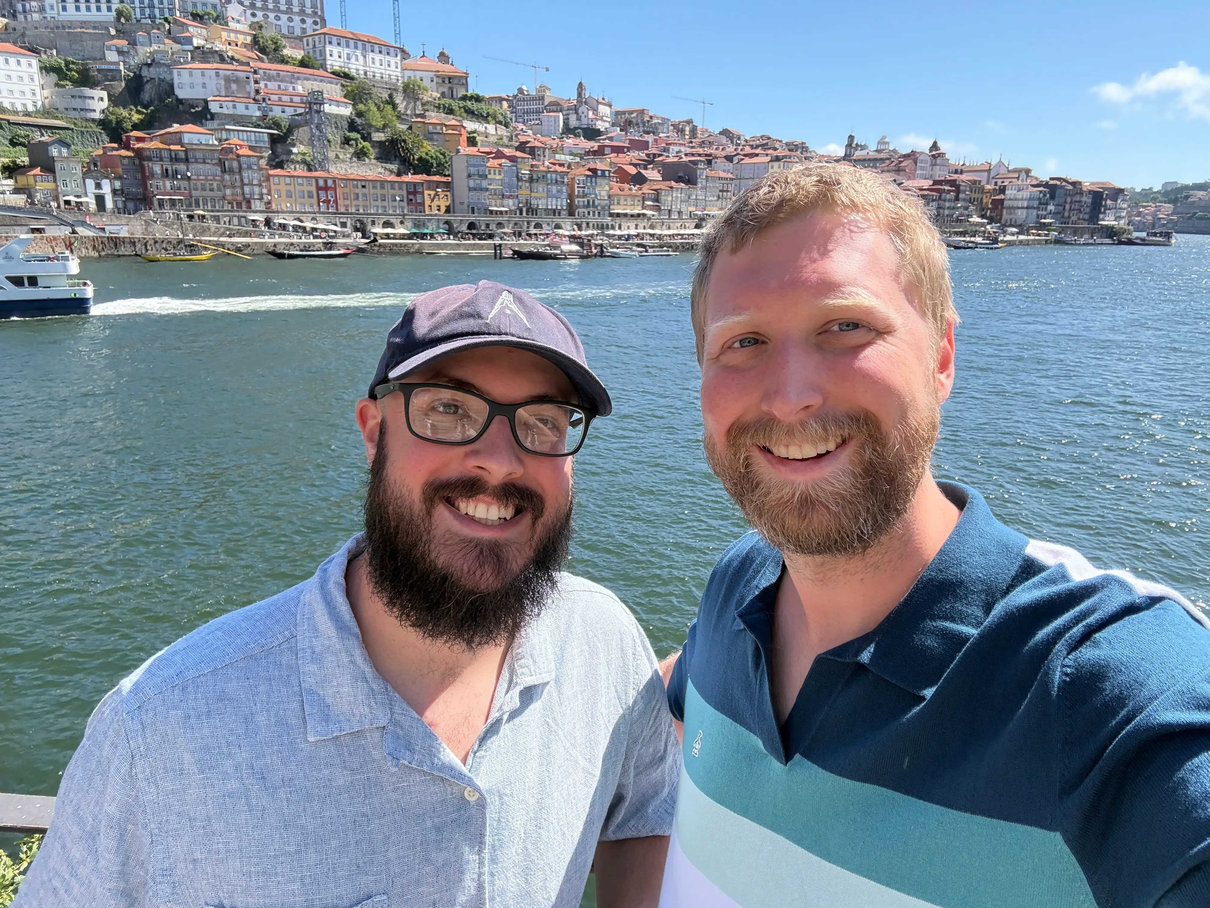 Two men in polo shirts smiling by water in Porto