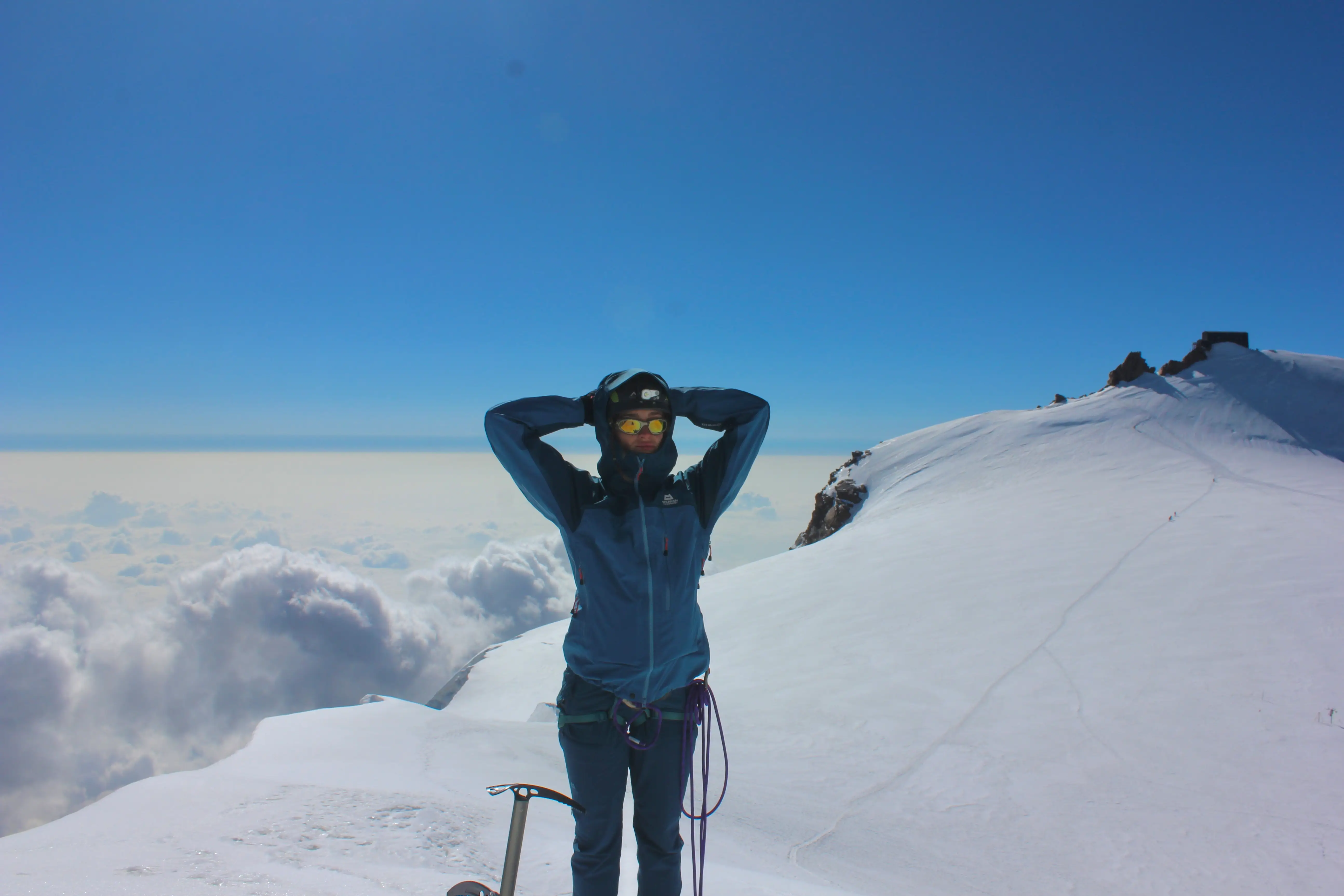 A woman in a blue mountaineering outfit stands on top of a snow-capped mountain.