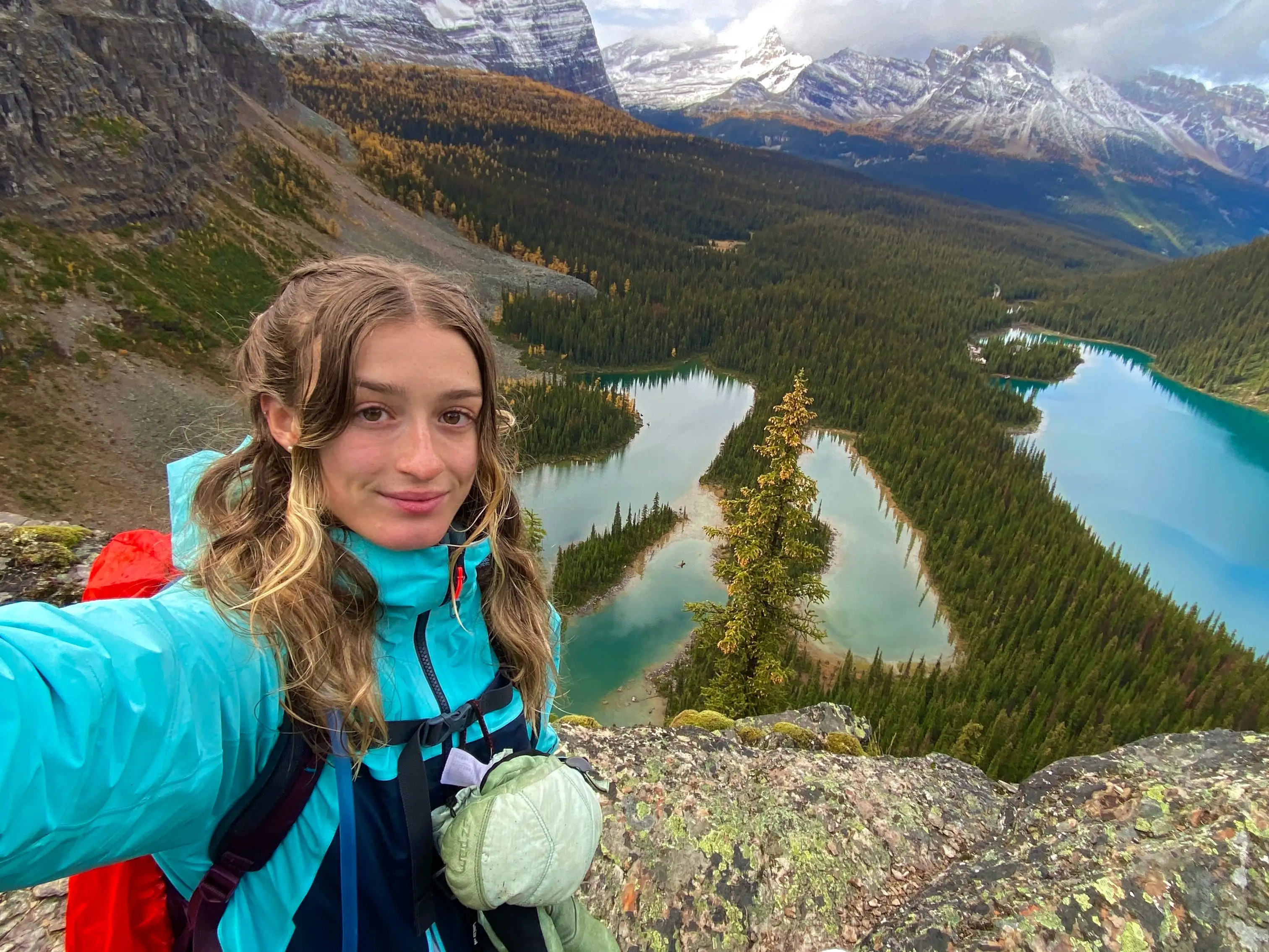 A woman takes a selfie on a mountain with two blue lakes in the background.