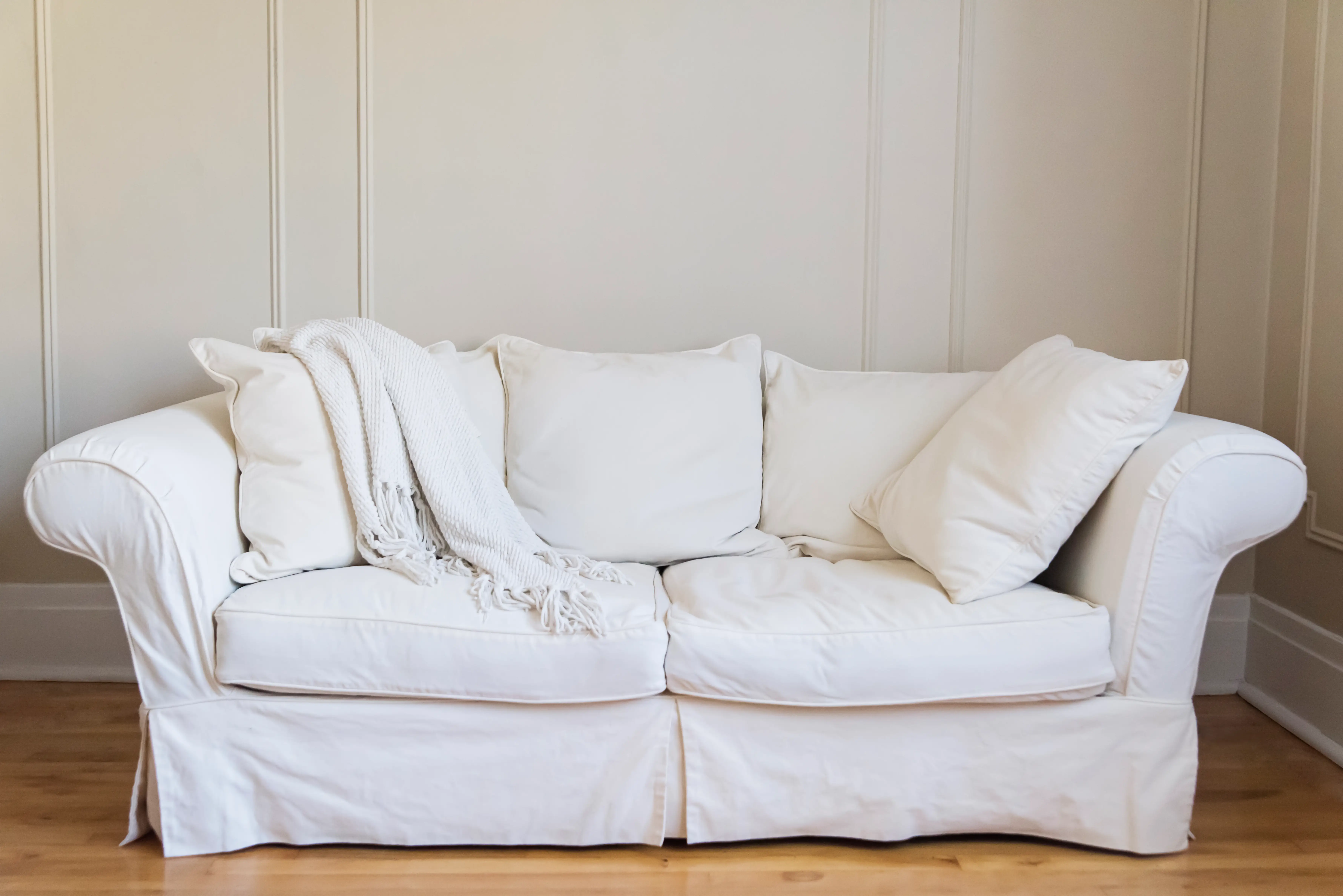 Cream slip-covered couch with matching pillows, blanket