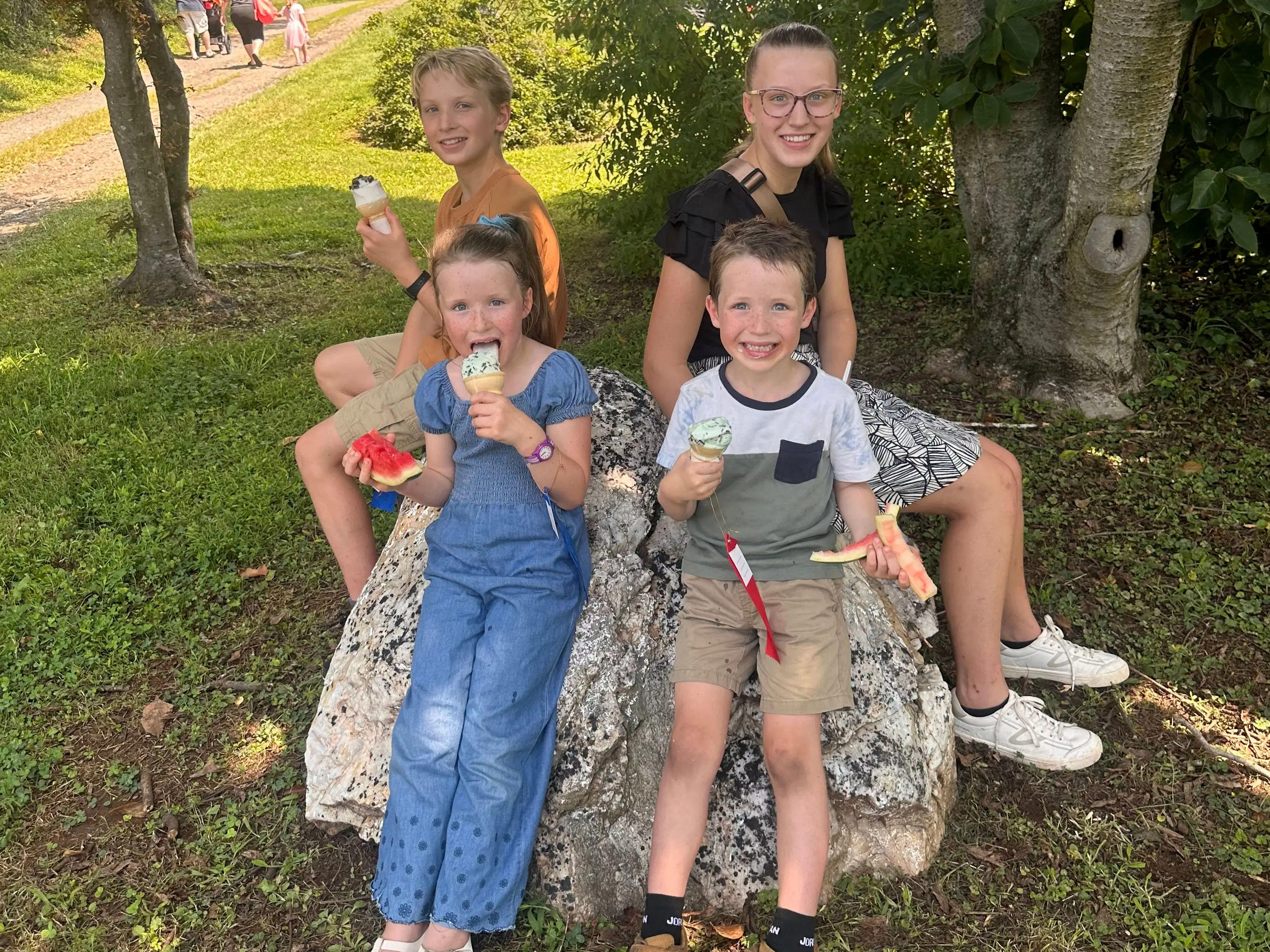 Four children are eating ice cream while sitting on a rock.