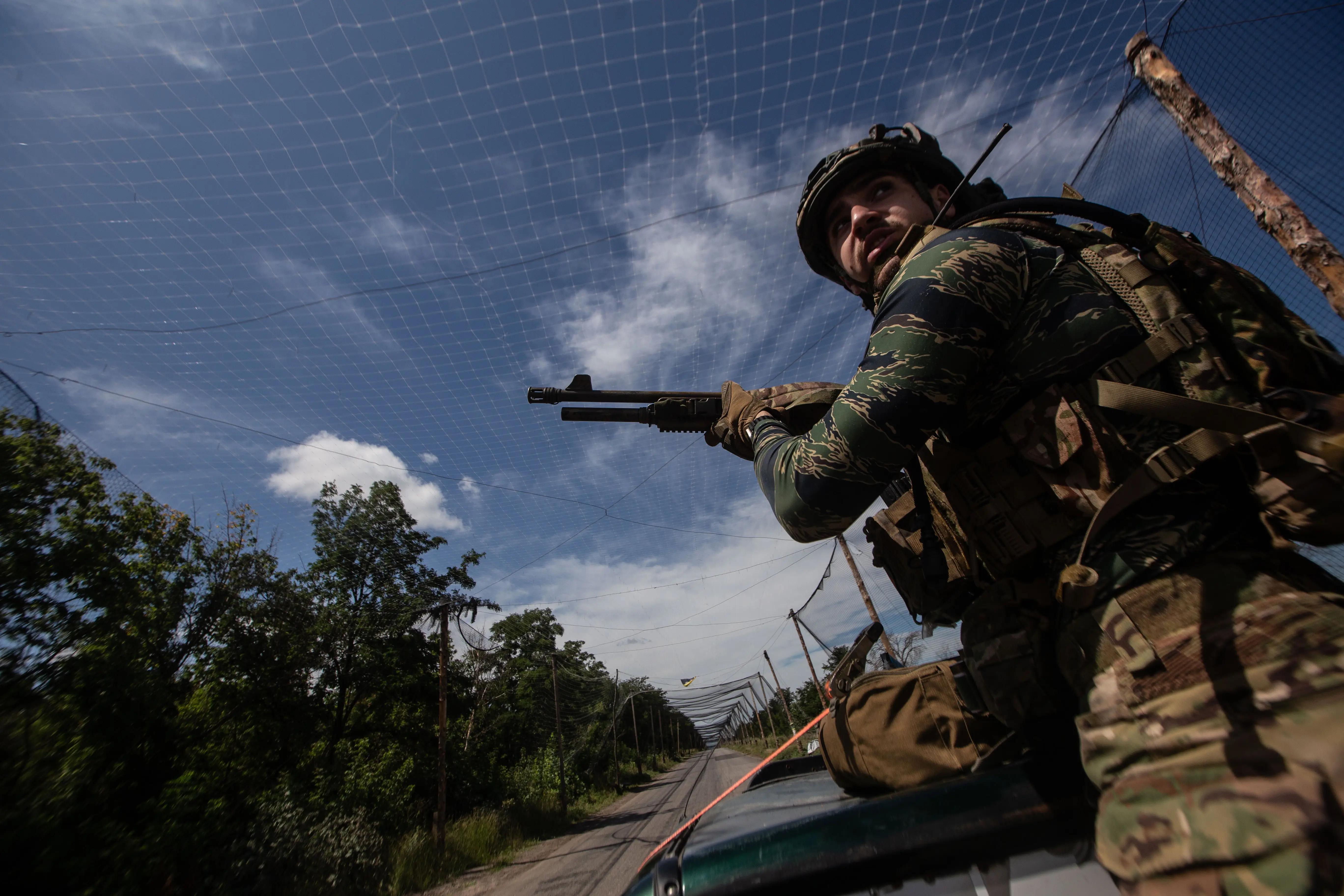 A Ukrainian soldier with an anti-drone shotgun inspects the area from the bed of a pick-up truck near Druzhkivka.