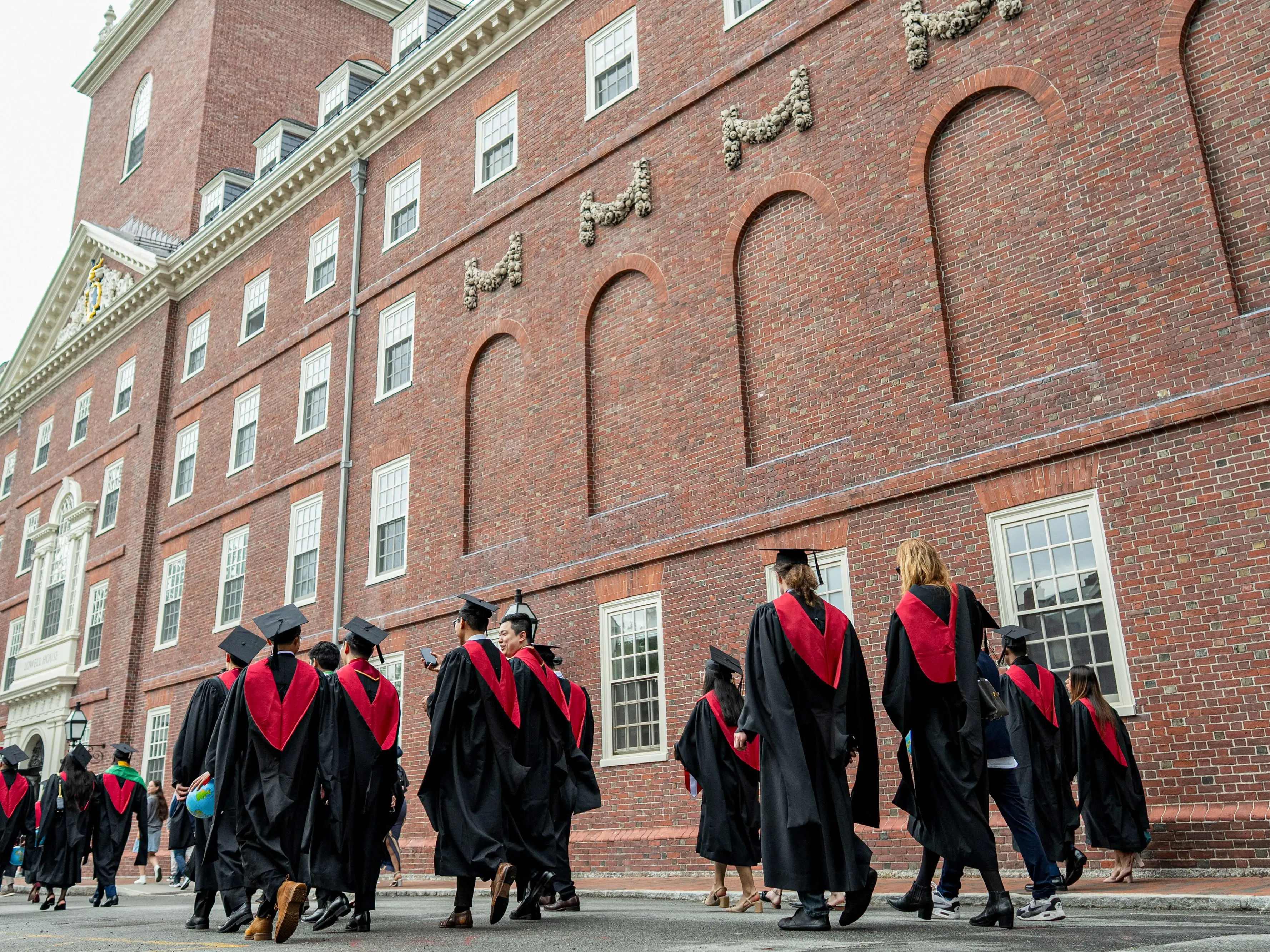 College graduates walk next to a brick building.