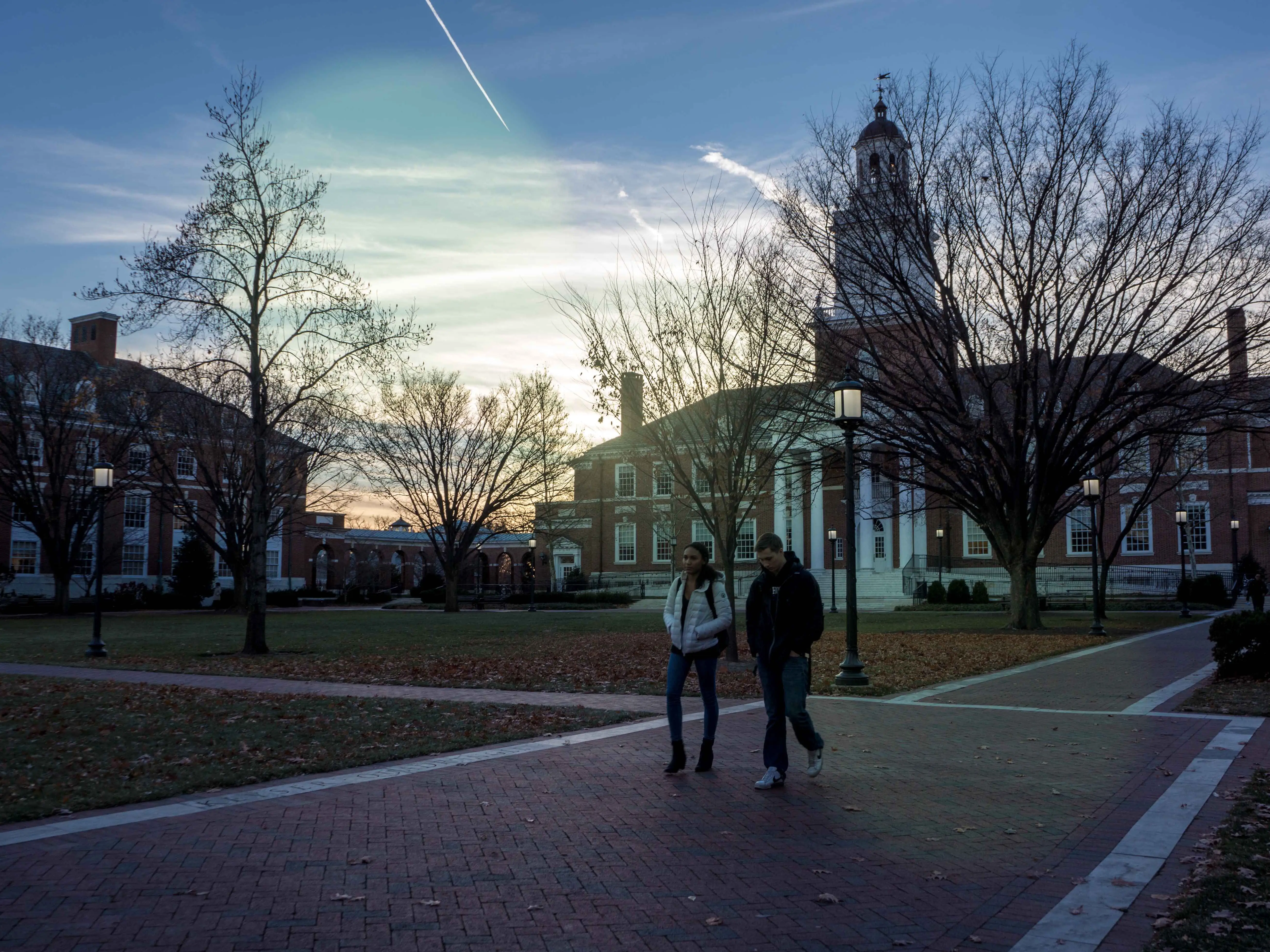 Two students walk on a college campus at sunset.