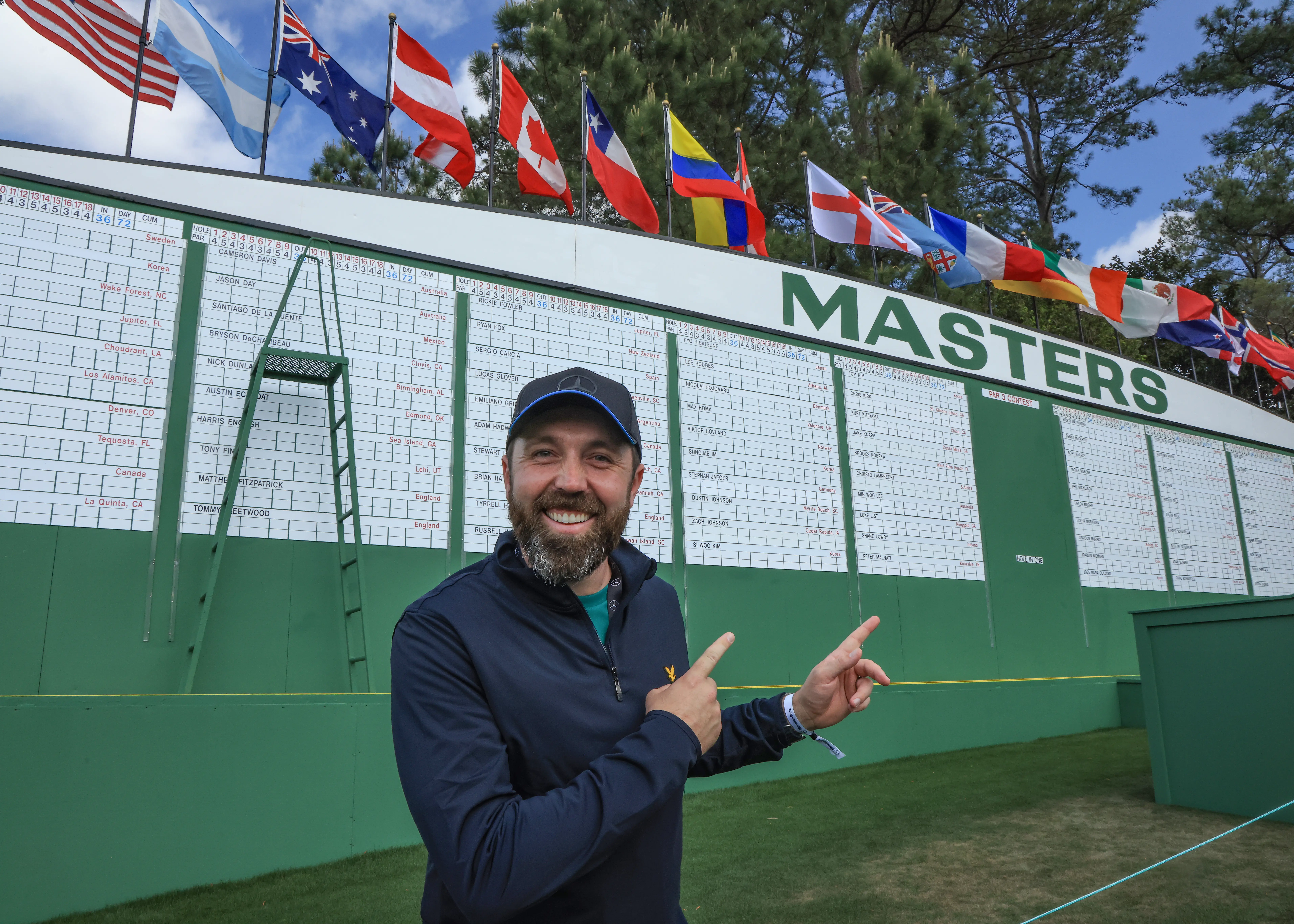 Rick Shiels, a bearded man stands in front of a scoreboard at the Masters golf tournament.