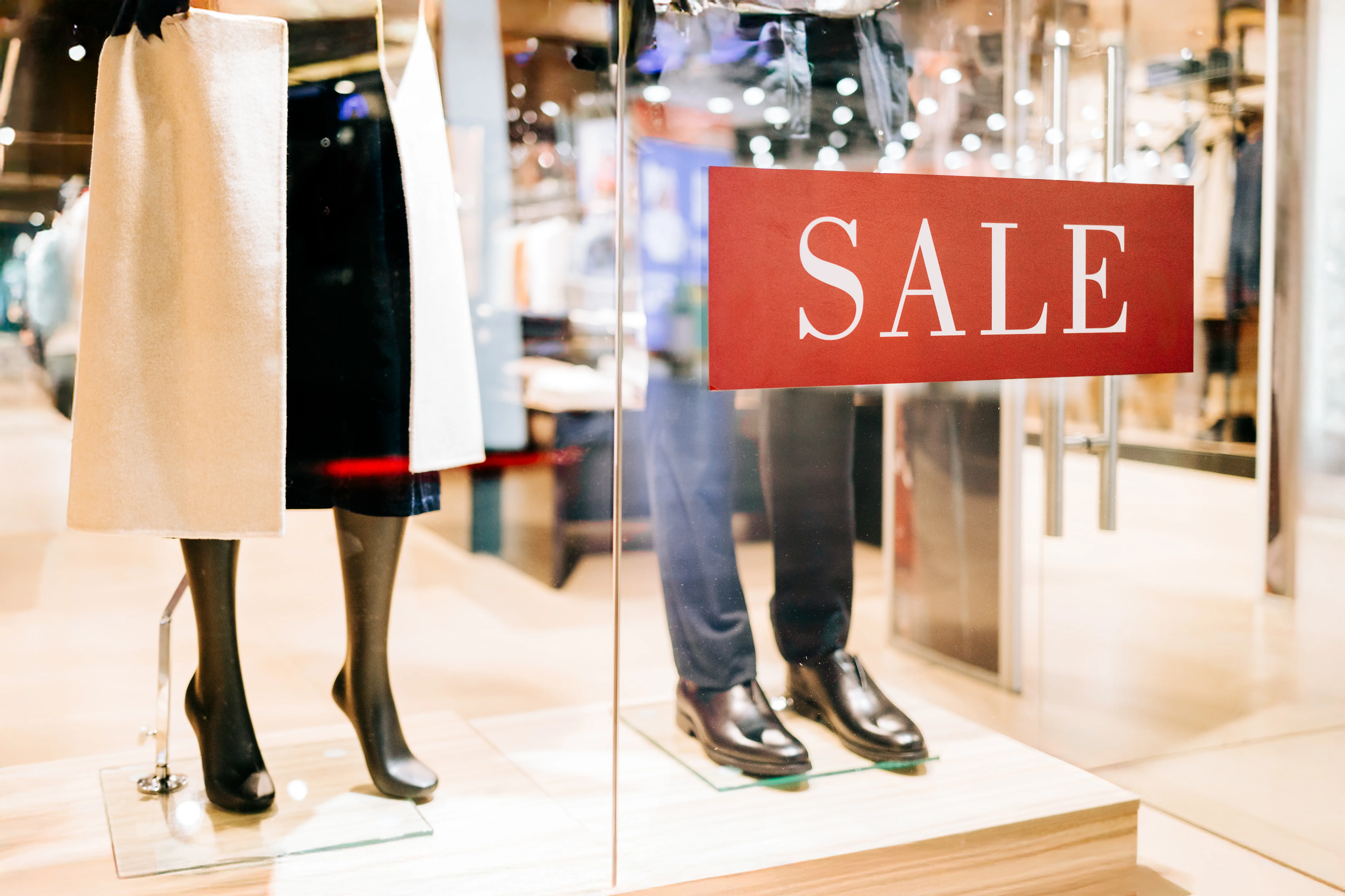 Mannequins wearing stylish clothes behind big red sale sign