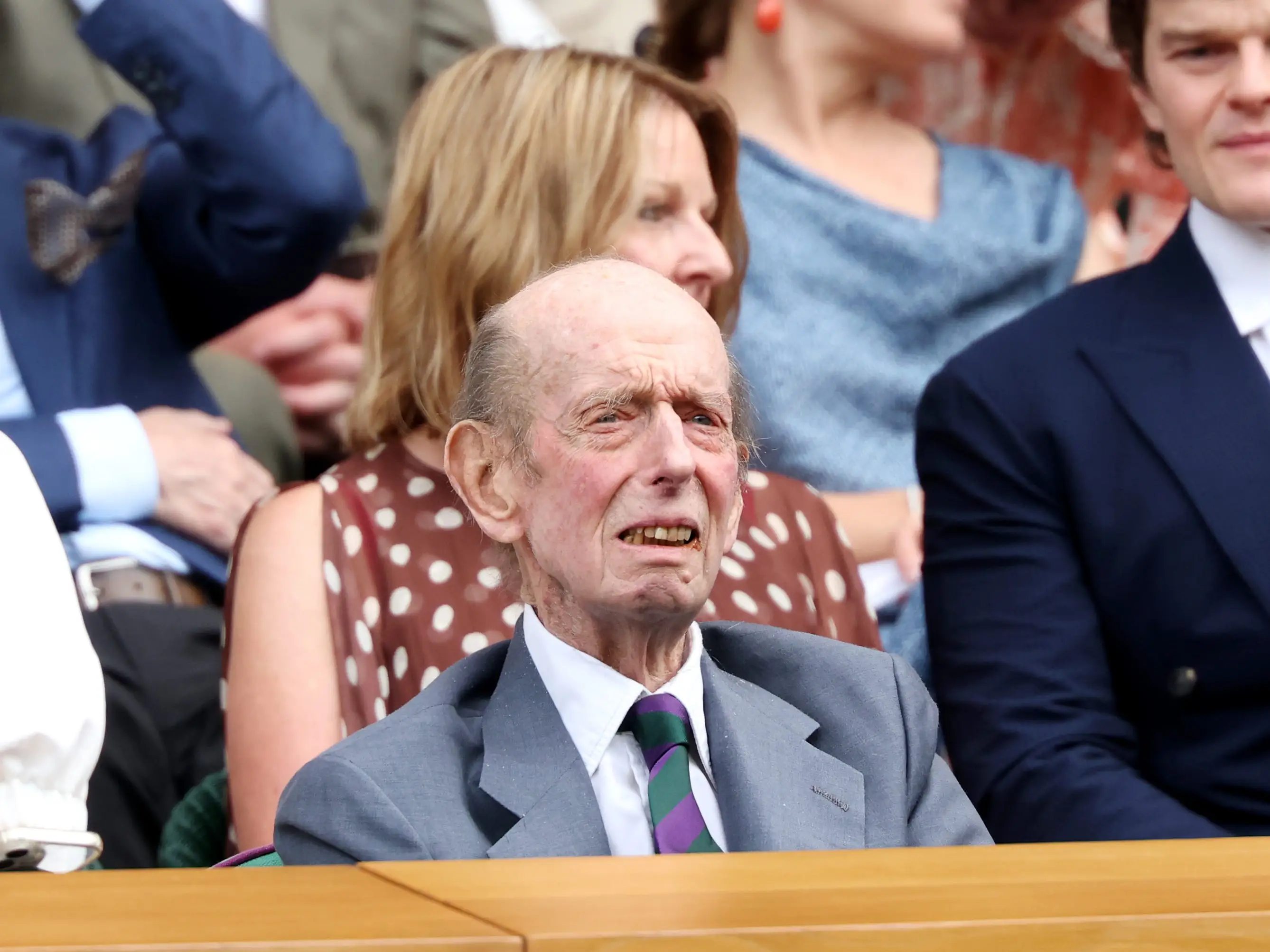 The Duke of Kent sits in a spectator box among other attendees at an outdoor event.