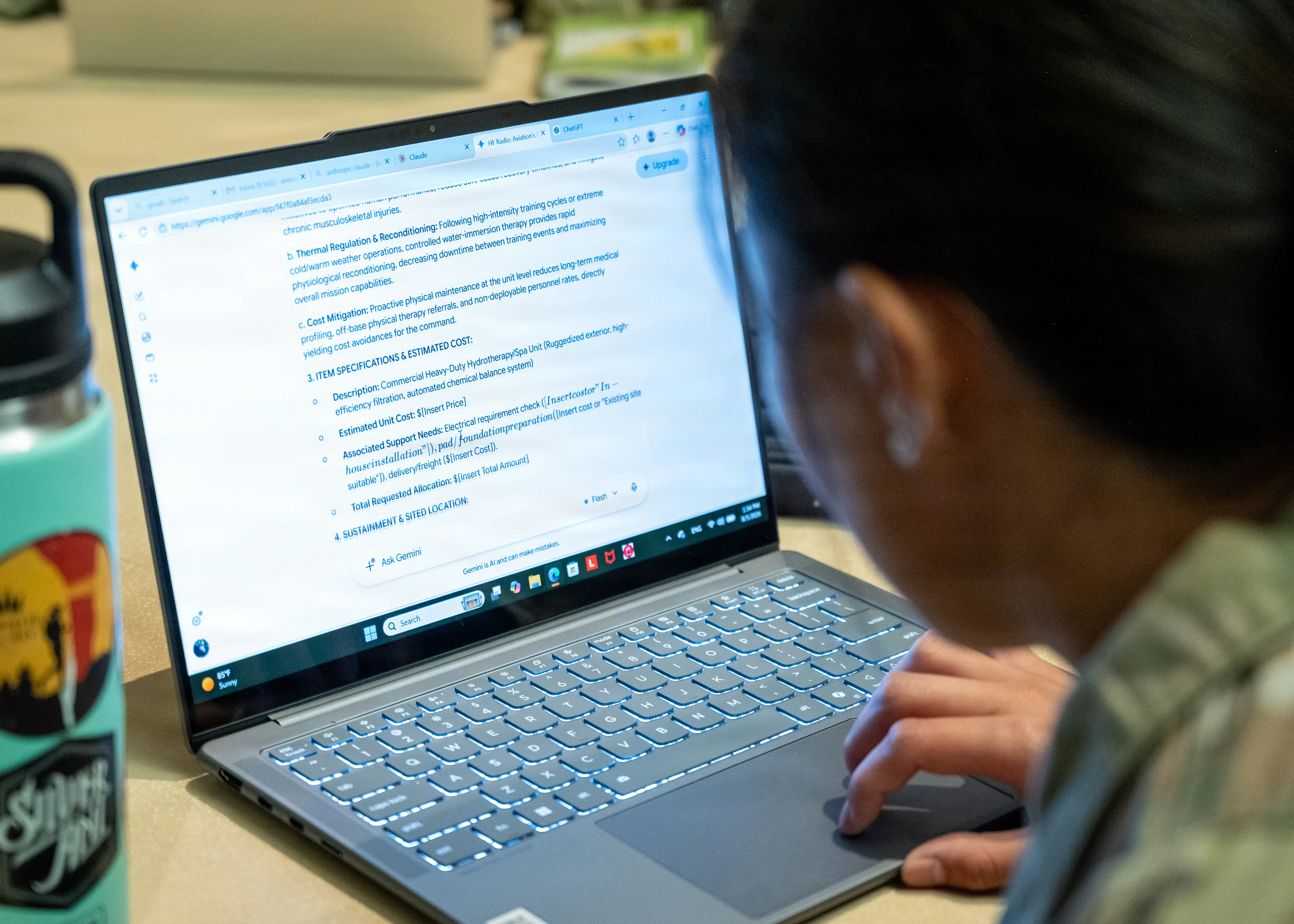 Person uses a laptop showing a Gemini-generated document beside a sticker-covered water bottle on a desk.