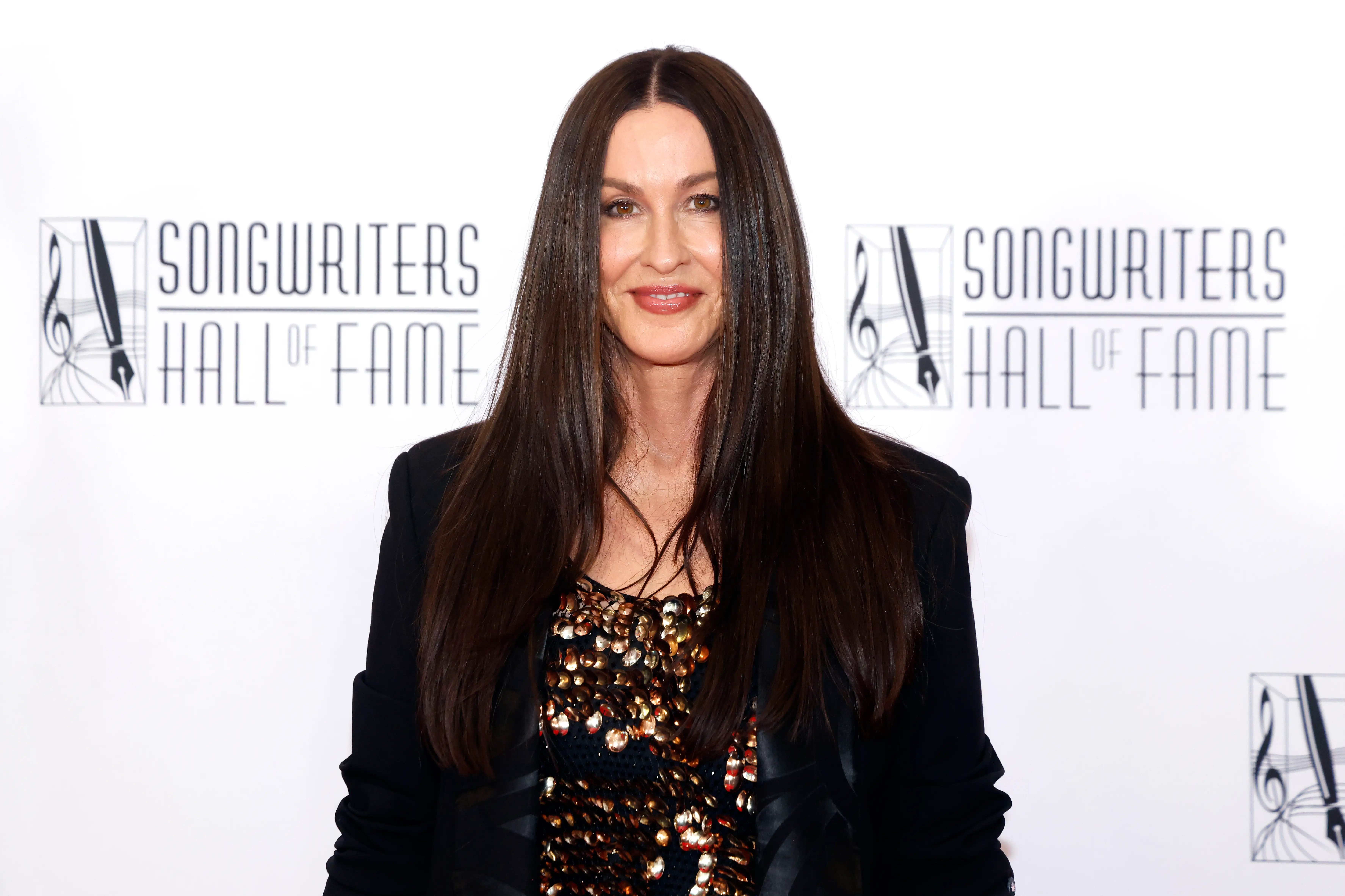 Alanis Morissette stands in front of a SONGWRITERS HALL OF FAME backdrop at an event.