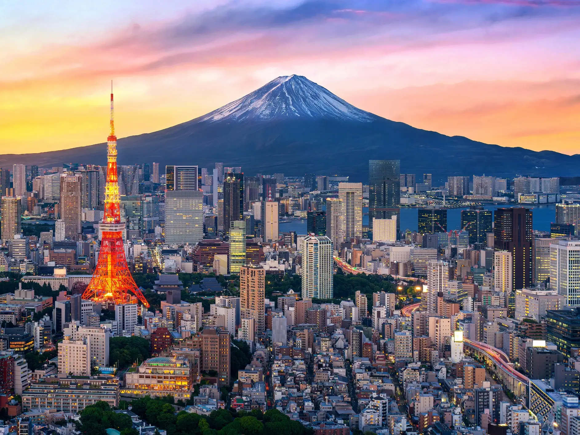 Tokyo skyline at sunset with illuminated Tokyo Tower and Mount Fuji rising in the background.