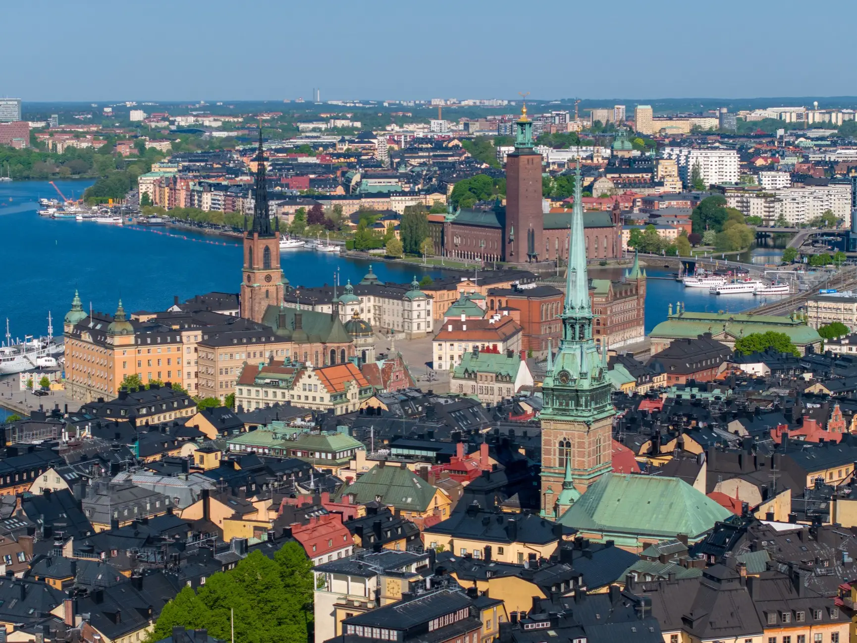 Aerial view of central Stockholm with Gamla Stan rooftops, church spires, waterfront, and Stockholm City Hall.