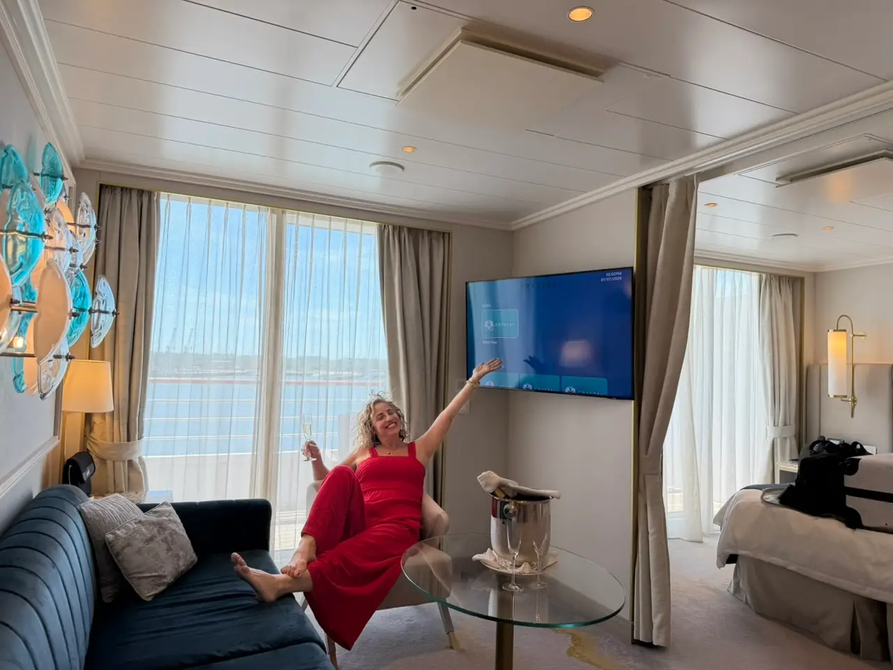 The author on board a cruise in her suite, pointing at the television