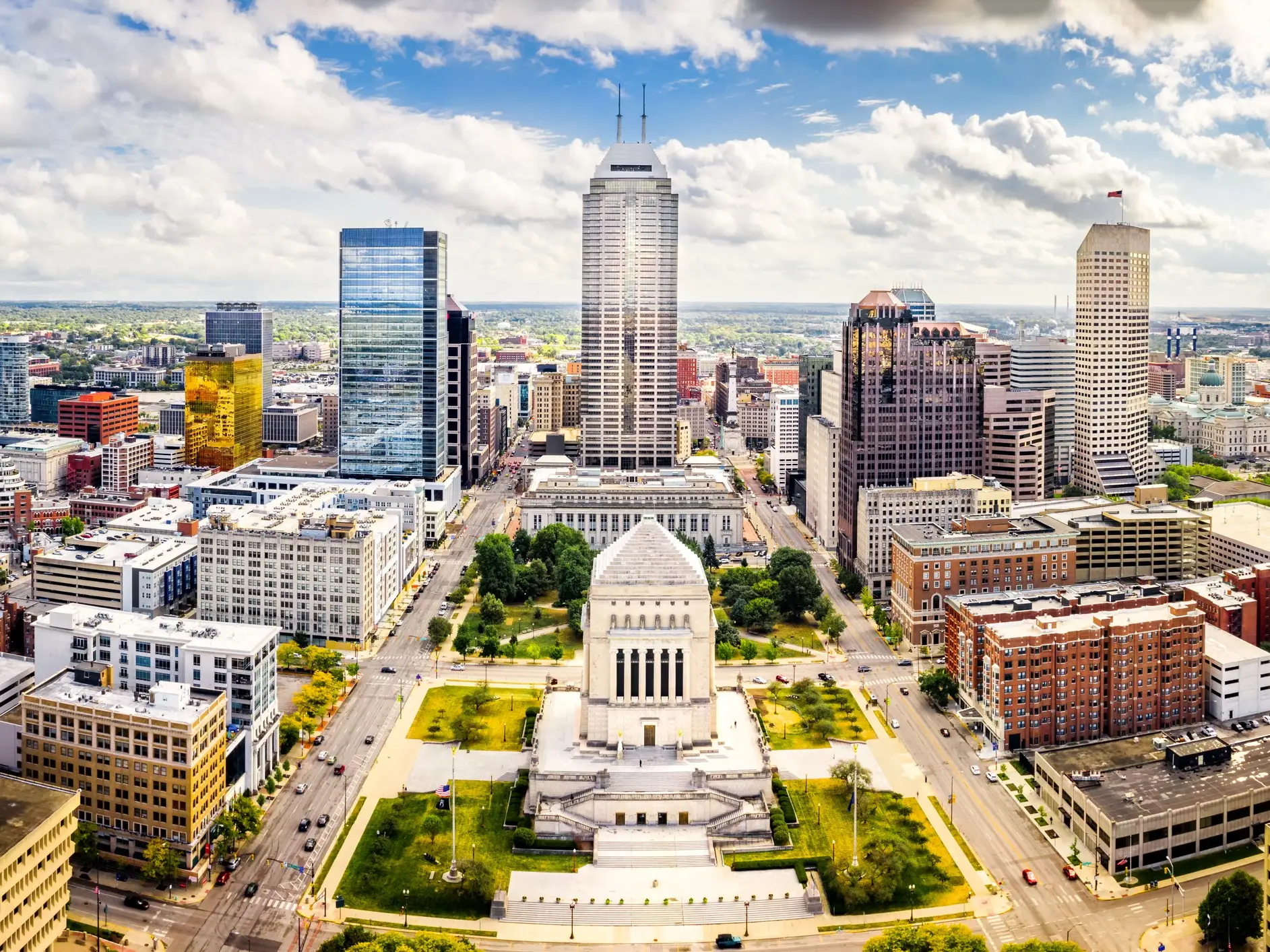 Downtown Indianapolis skyline surrounds the Indiana World War Memorial beneath a partly cloudy sky.