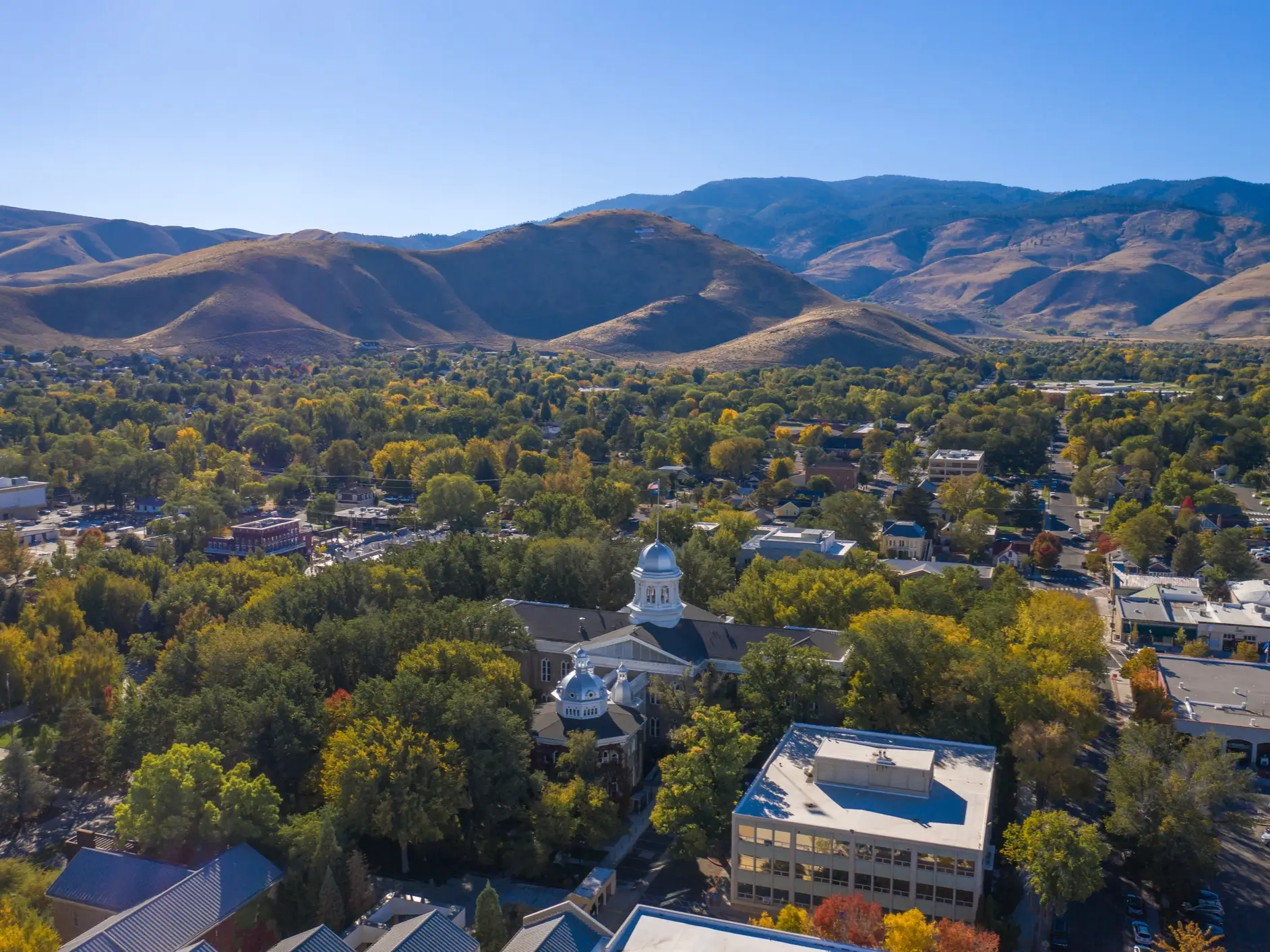 Aerial view of the Nevada State Capitol amid trees with dry mountains beyond.