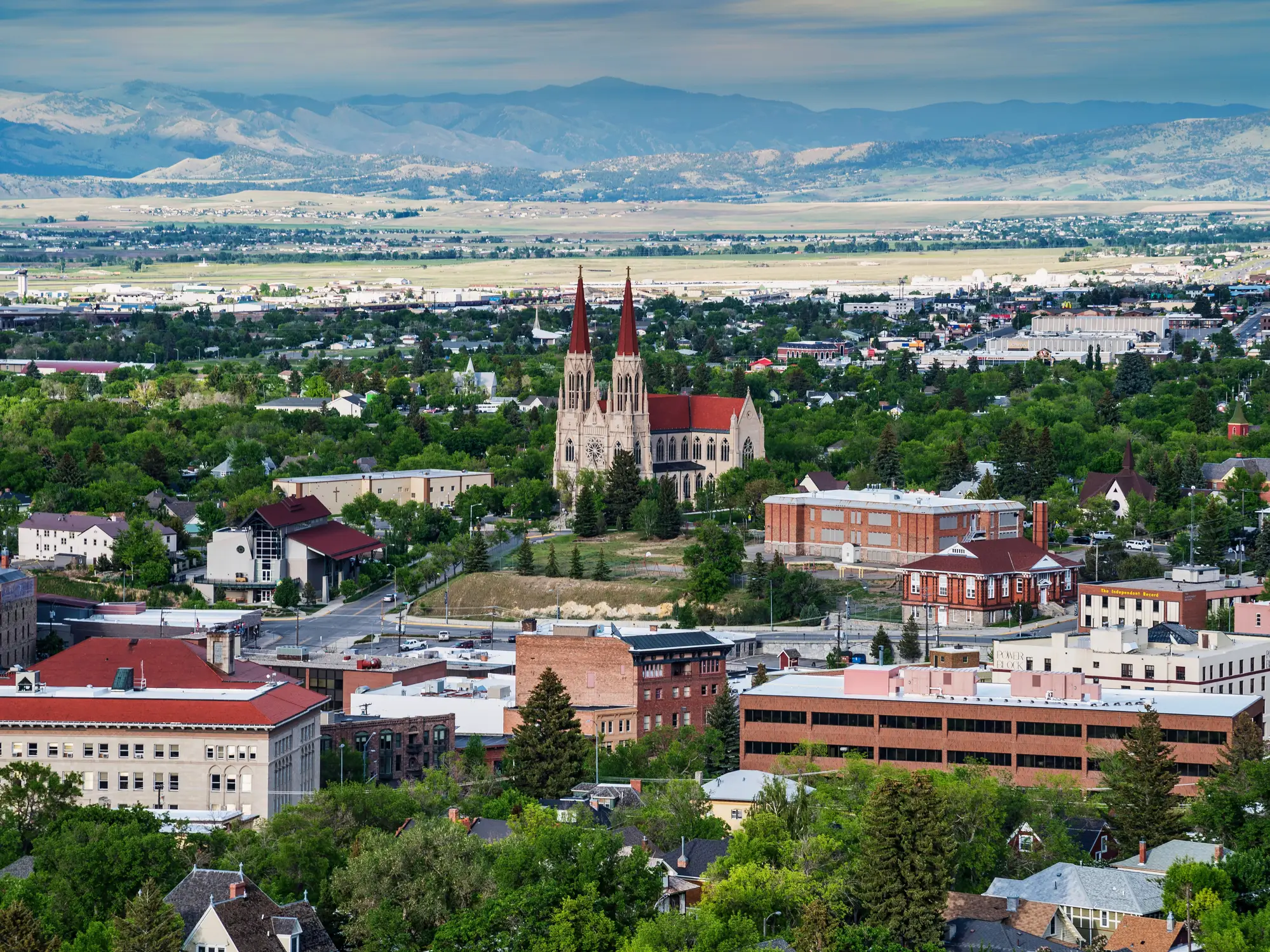 Aerial view of downtown Helena with the Cathedral of Saint Helena, surrounding buildings, trees, and mountains.