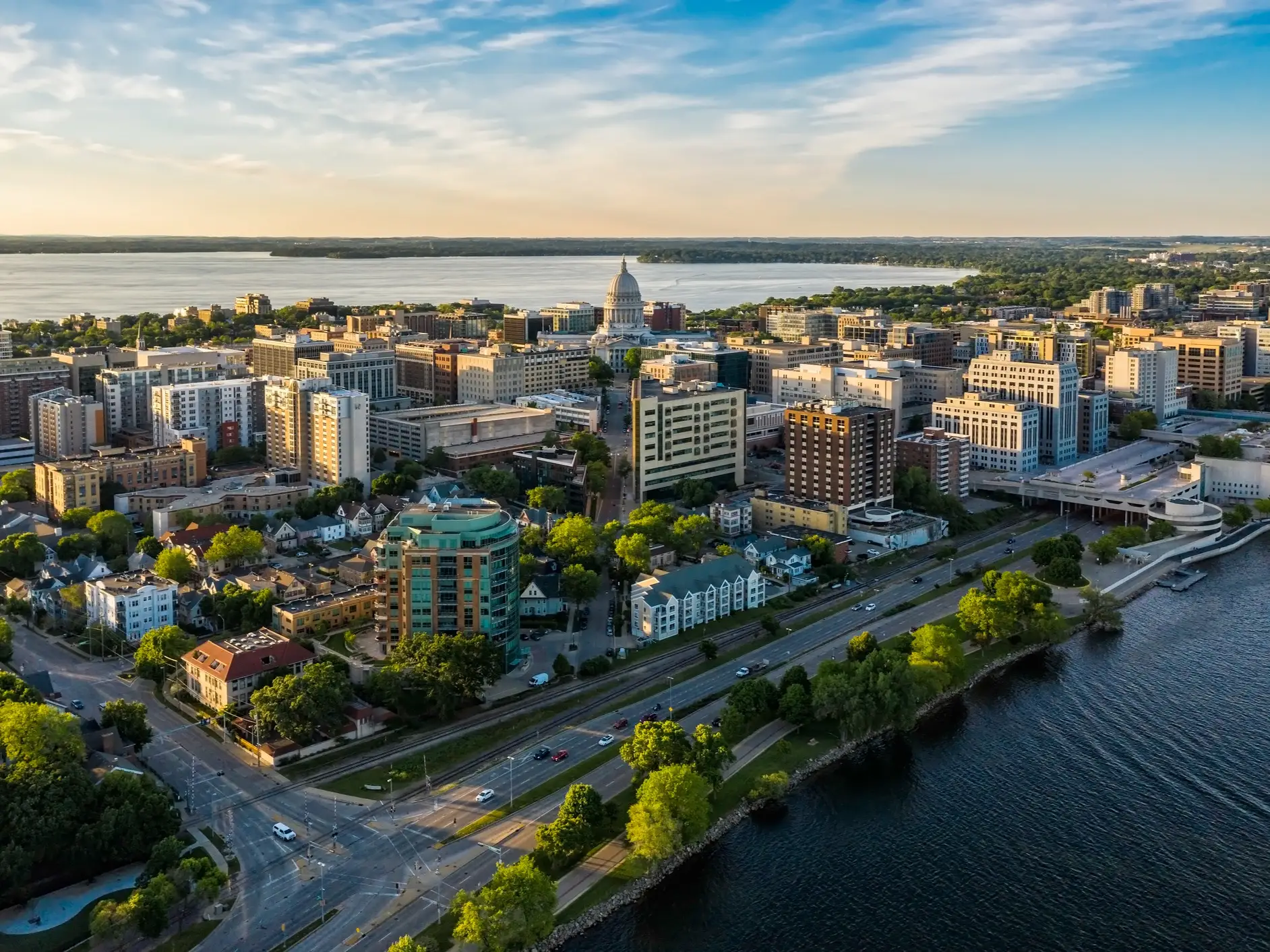 Aerial view of downtown Madison with the Wisconsin State Capitol between lakes in warm evening light.