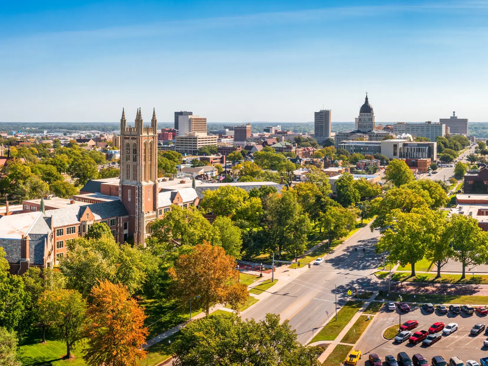 Downtown Topeka skyline with the Kansas State Capitol dome, church towers, tree-lined streets, and parked cars.