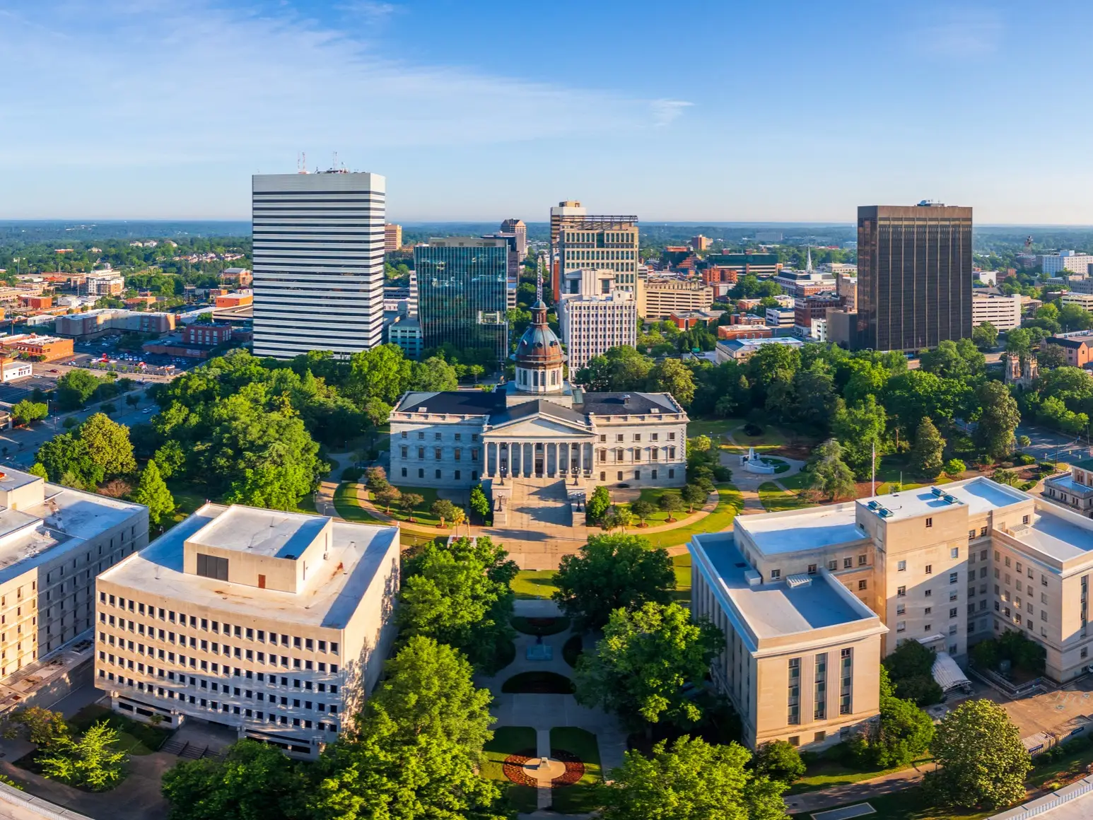 Aerial view of the South Carolina State House surrounded by trees and downtown Columbia buildings.