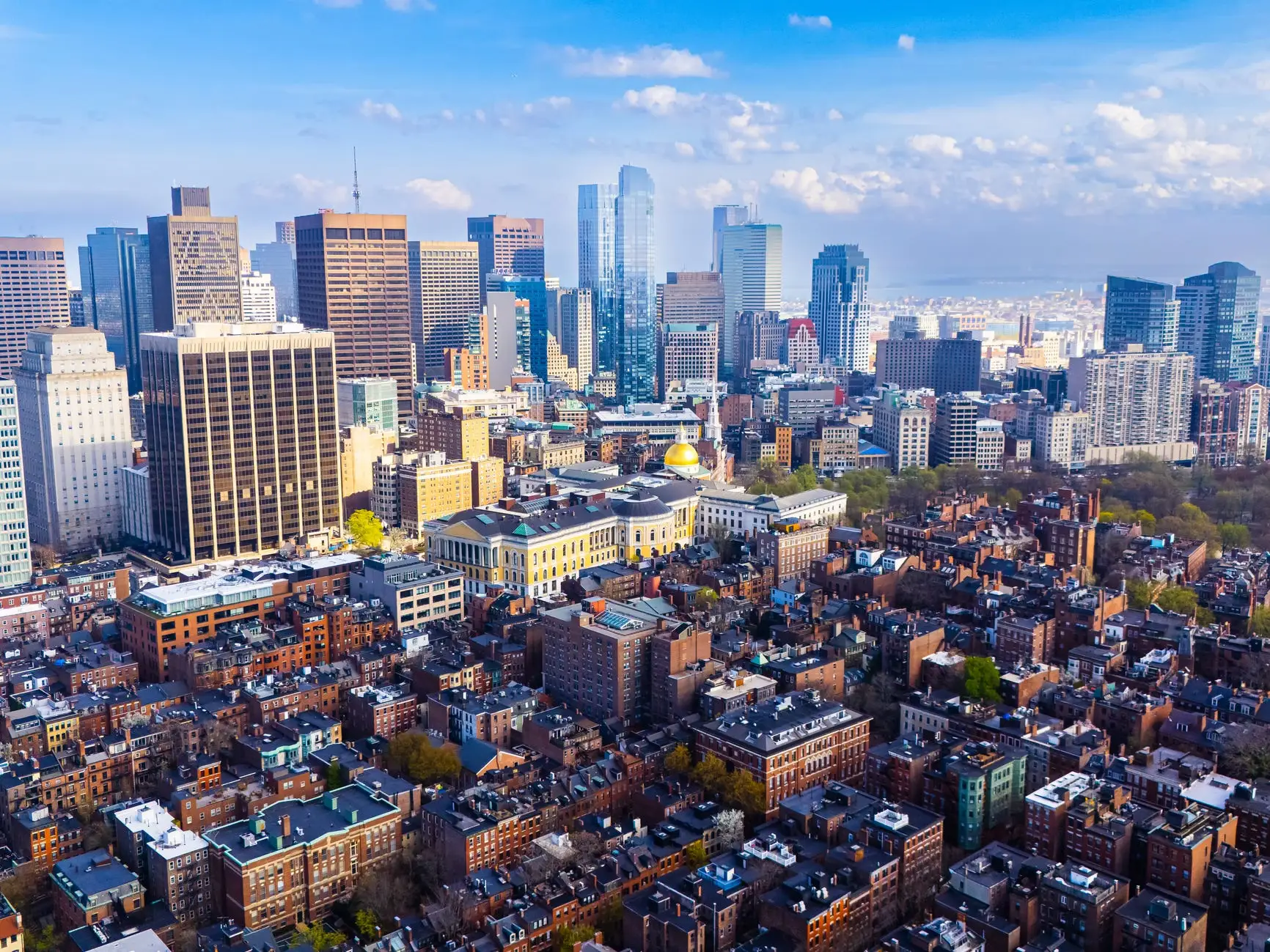 Aerial view of Boston with skyscrapers visible in the background and orange-brick houses in the foreground.