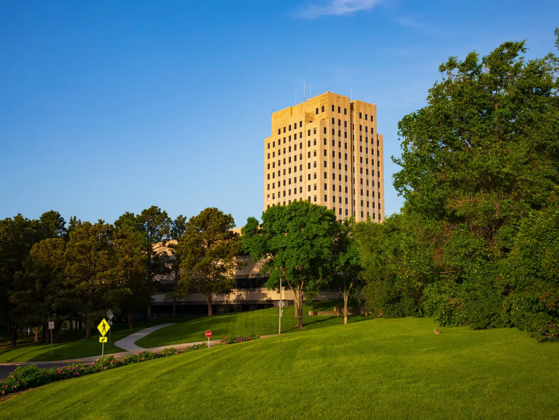 North Dakota State Capitol tower rises above green lawns and trees under a clear blue sky.
