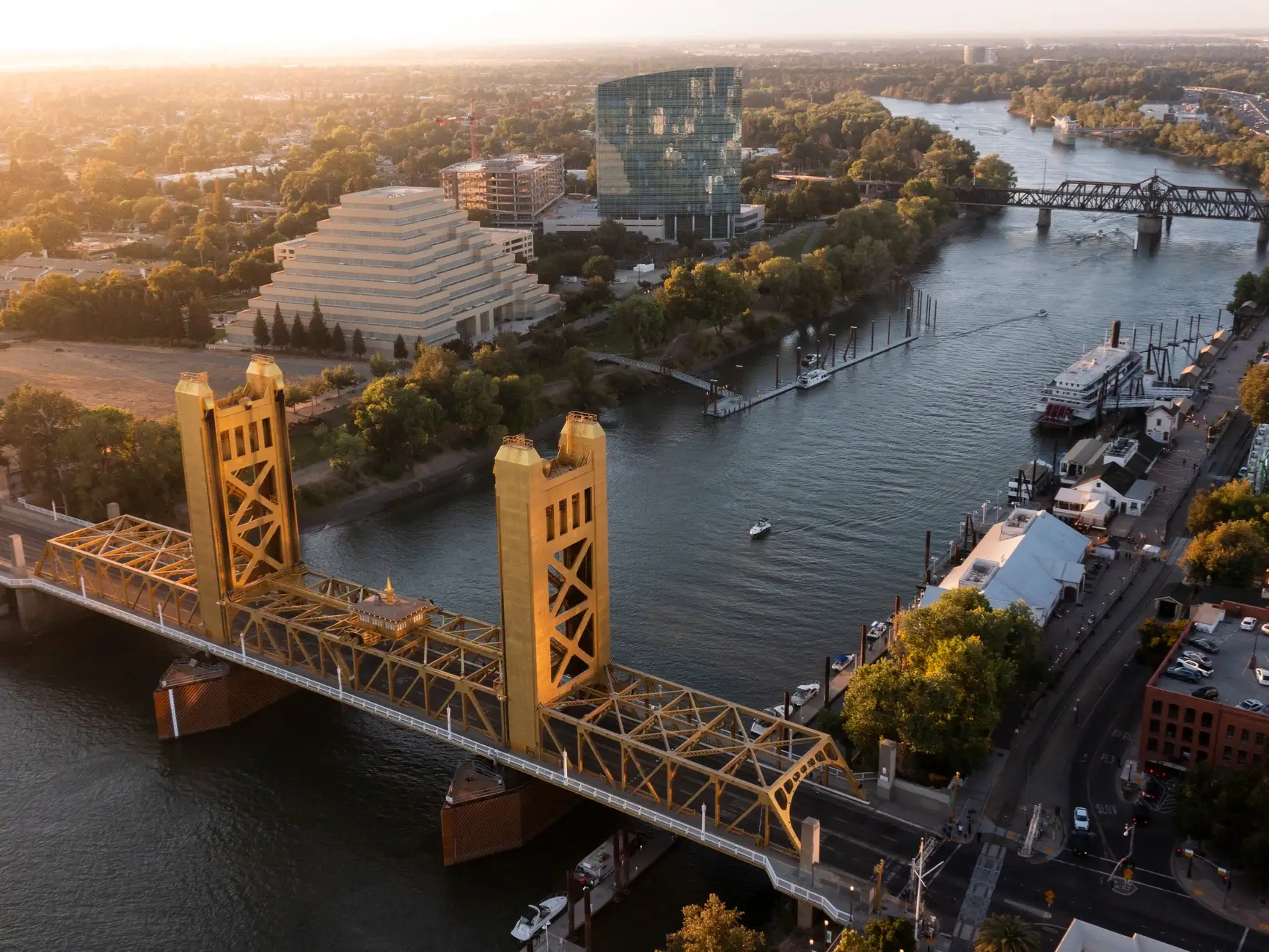 Aerial view of Sacramento’s Tower Bridge spanning the Sacramento River near waterfront buildings at sunset.
