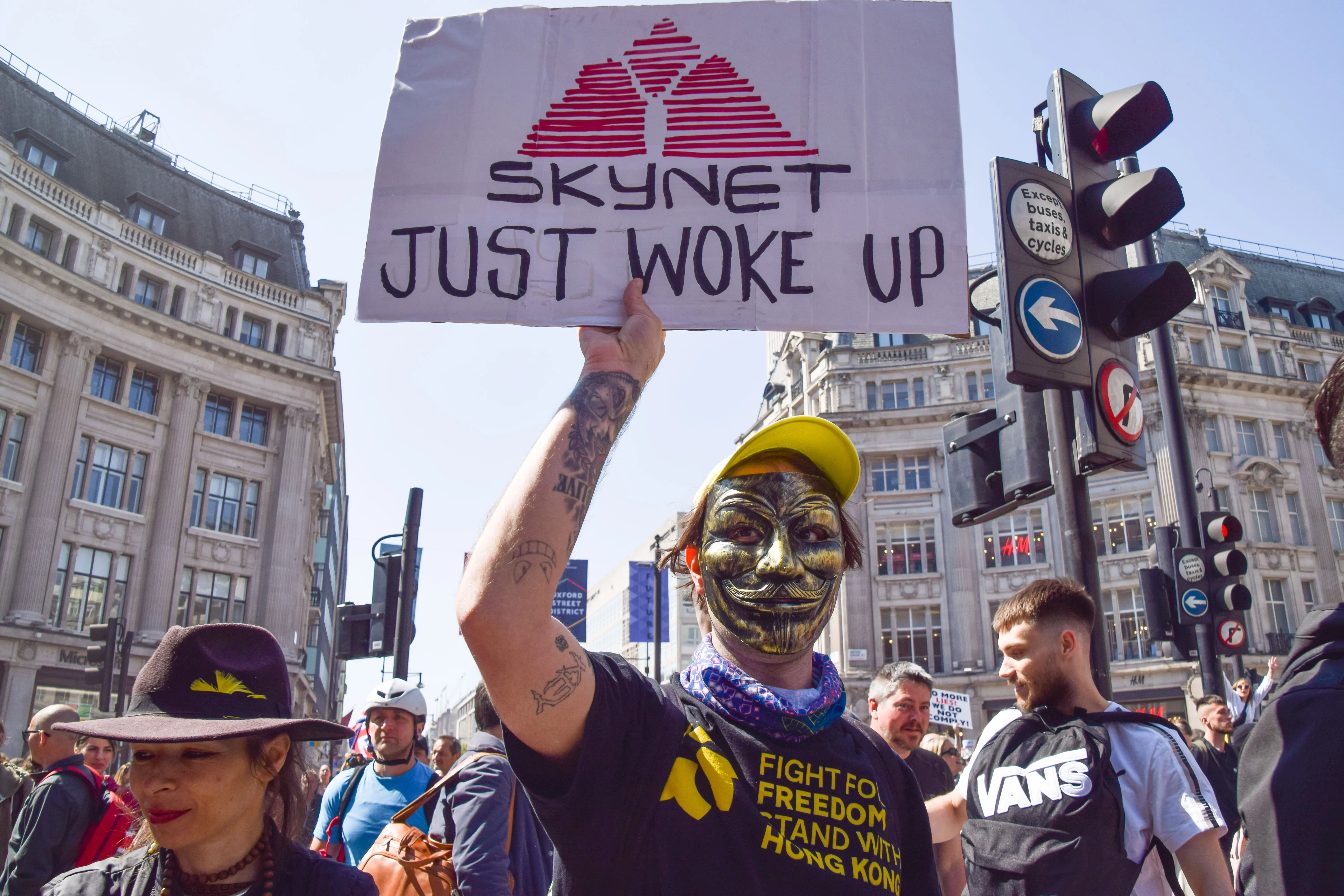 A masked protester holds a placard saying 'Skynet Just Woke Up' in reference to the Terminator movies in London during a 2021 anti-lockdown demonstration.