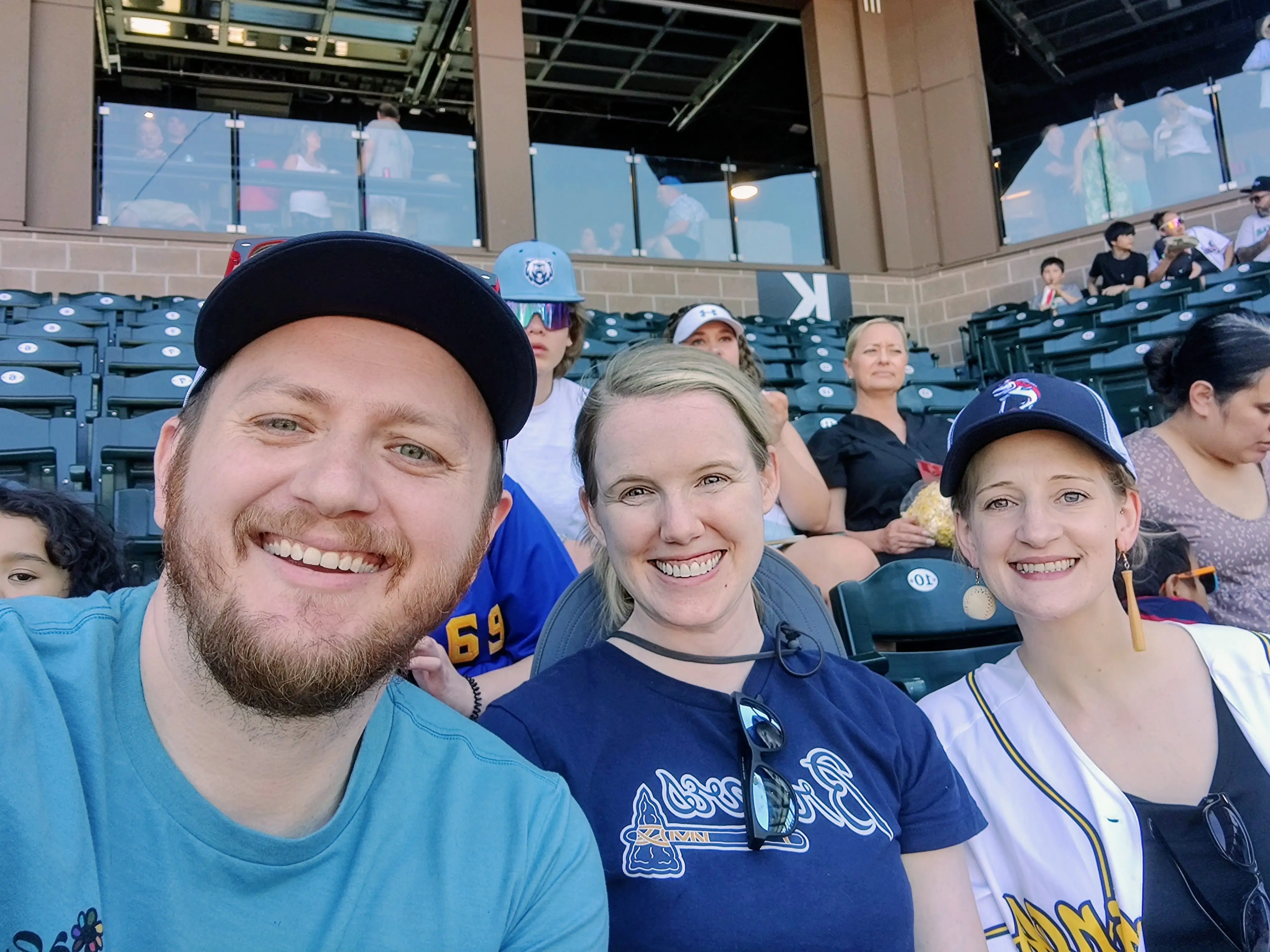 Laura Grace, her husband, and their friend pose for a photo at a baseball game.