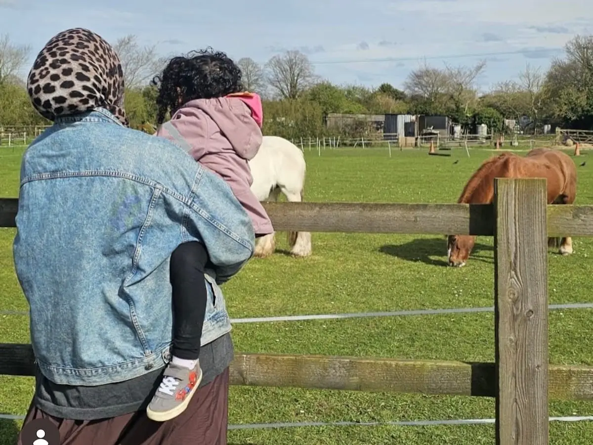The author holds her young daughter while looking at horses on a farm.