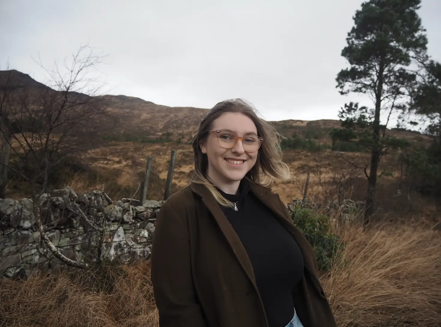 The writer wearing a brown jacket and standing in front of nature on the remote Isle of Rum.